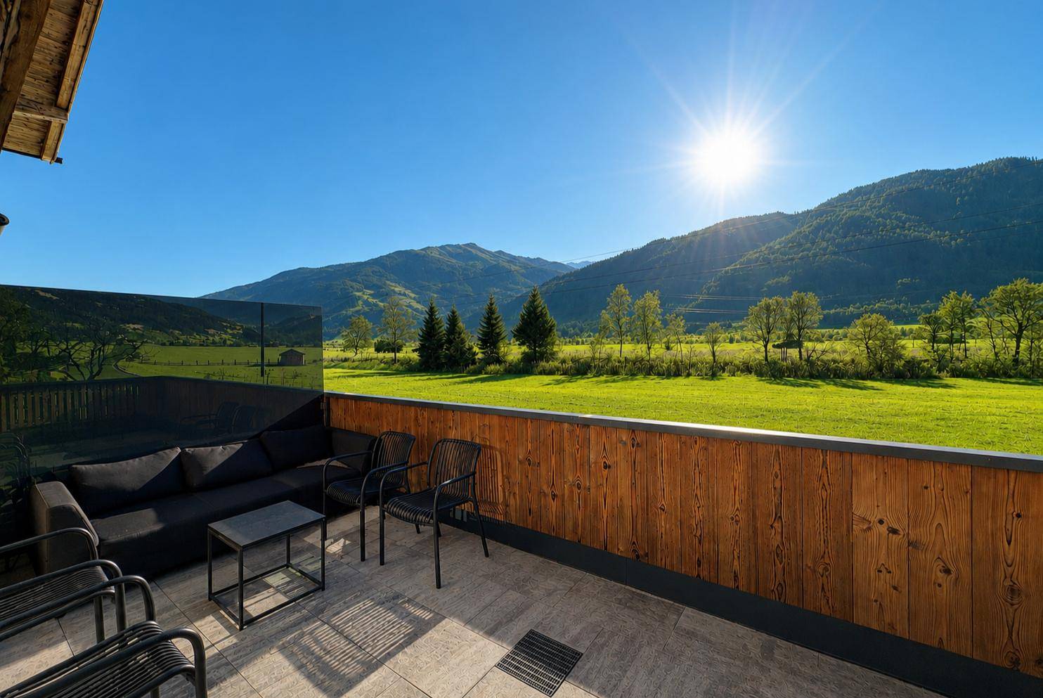 Sonnige Terrasse mit bequemen Sitzmöbeln und weitem Blick auf grüne Wiesen und Berge.