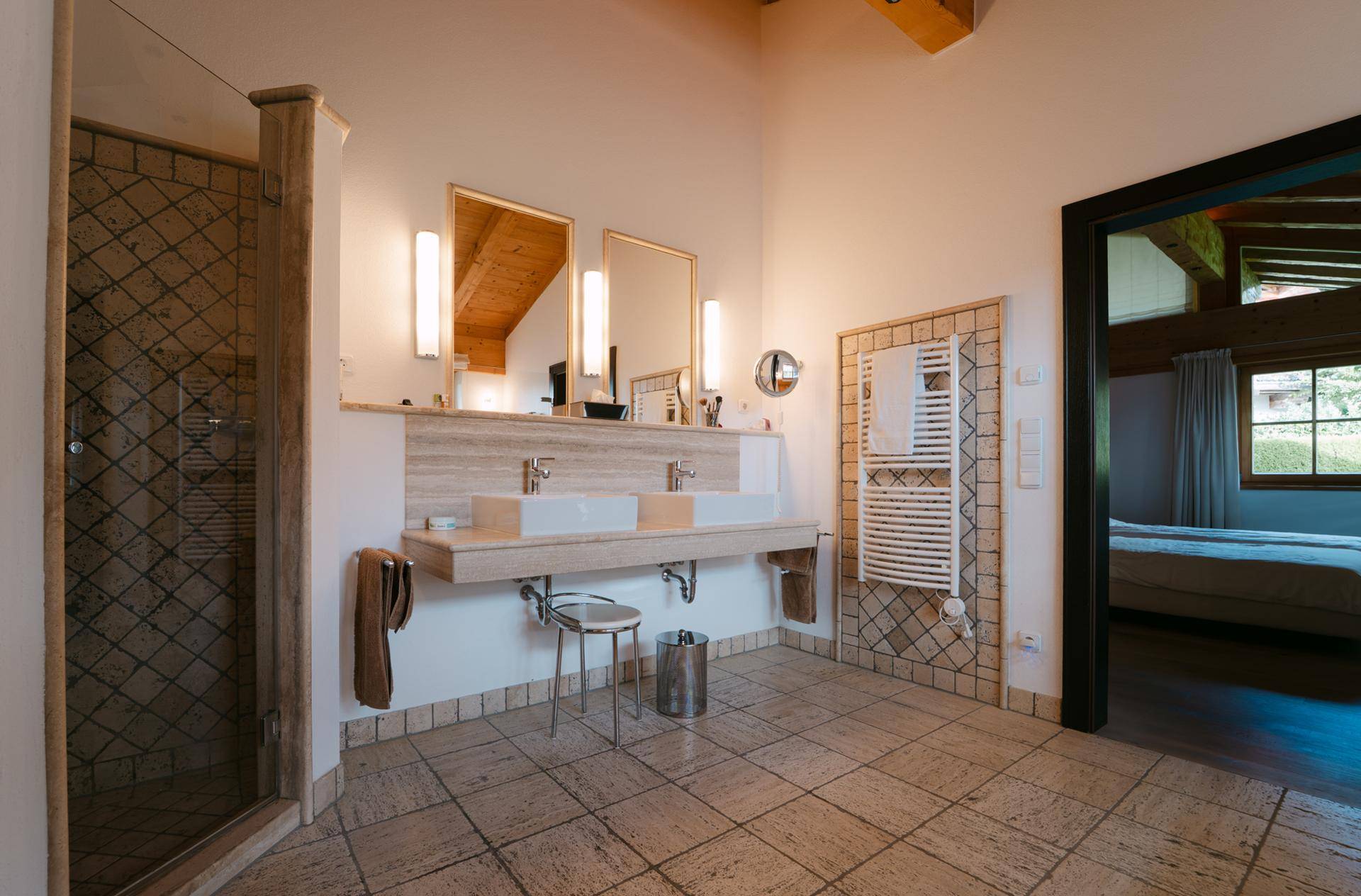 Modernes Badezimmer mit Doppelwaschbecken, begehbarer Dusche und Fliesenboden in Natursteinoptik.