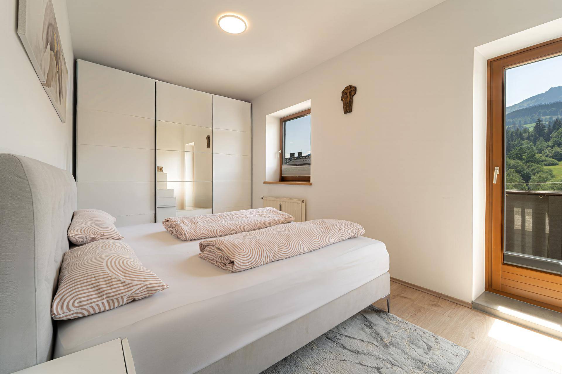 Schlafzimmer mit Doppelbett, Spiegelschrank und Zugang zu einem Balkon mit Bergblick.