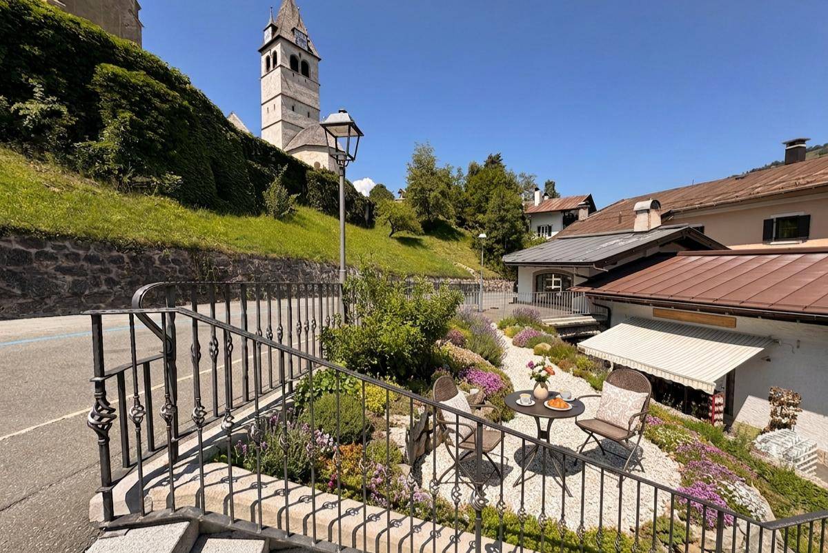 Gemütliche Außenterrasse mit Sitzgelegenheiten, Blumen und Blick auf die Kirche und Umgebung.