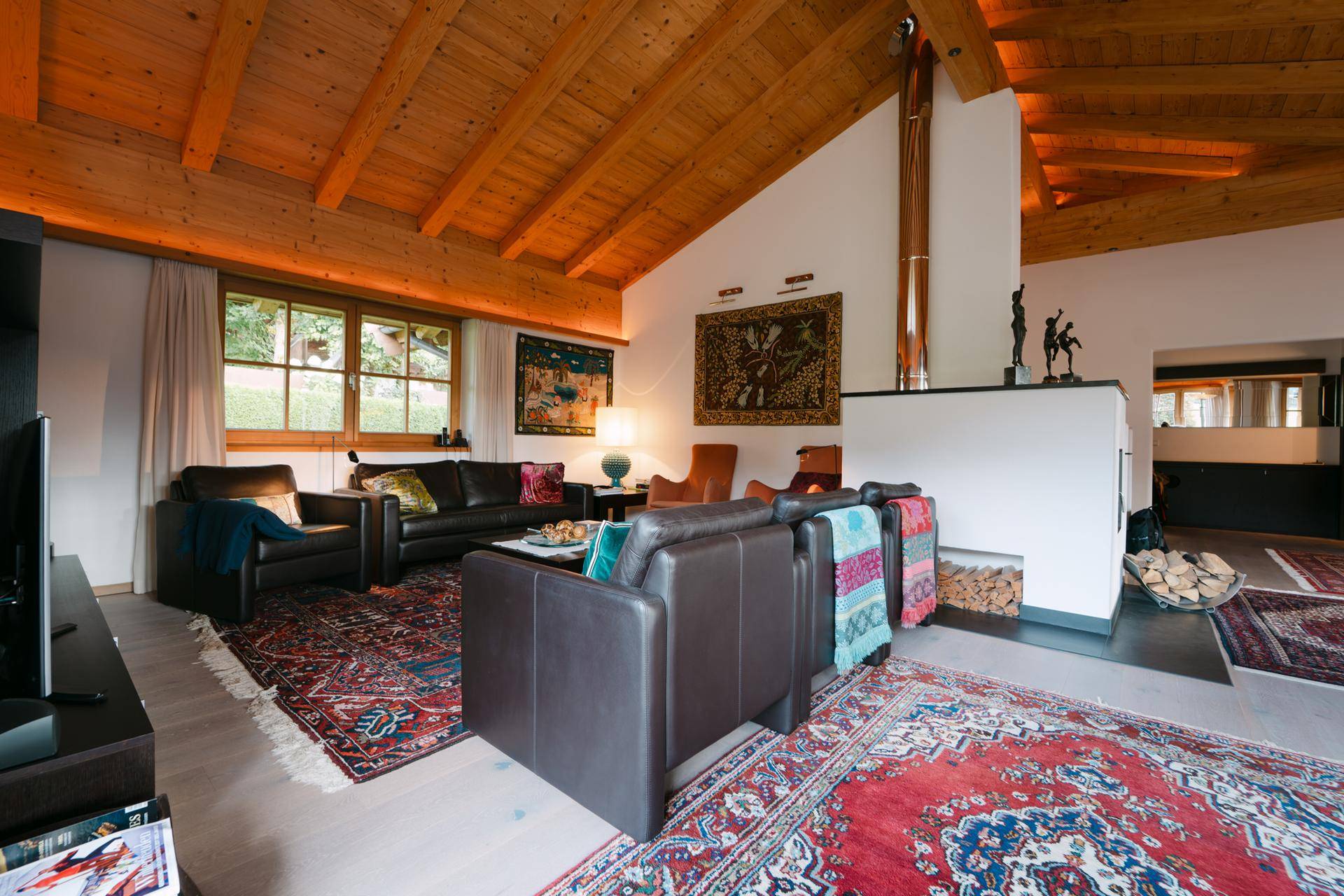 Gemütliches Wohnzimmer mit Holzbalkendecke, Kamin und bequemen Ledersofas, dekoriert mit Teppichen.