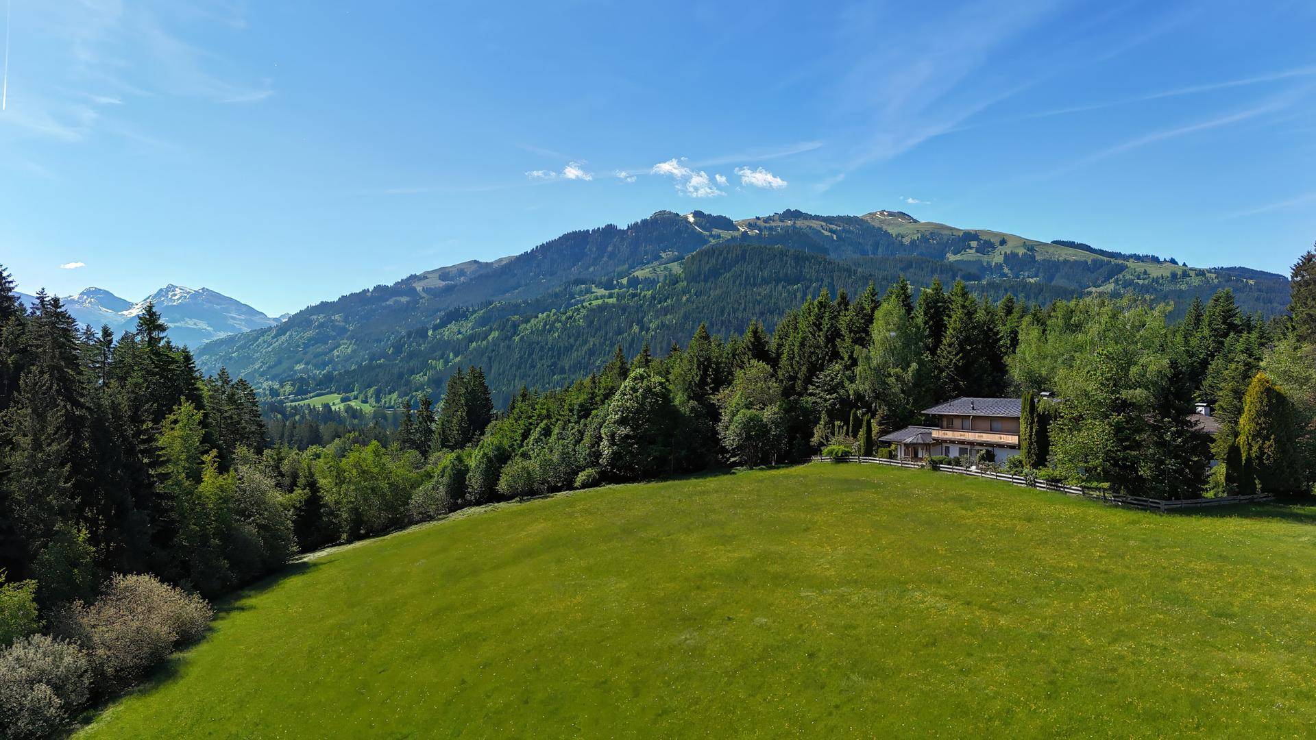 Weitläufige Landschaft mit grünen Wiesen, dichten Wäldern und einem Haus in der Ferne.