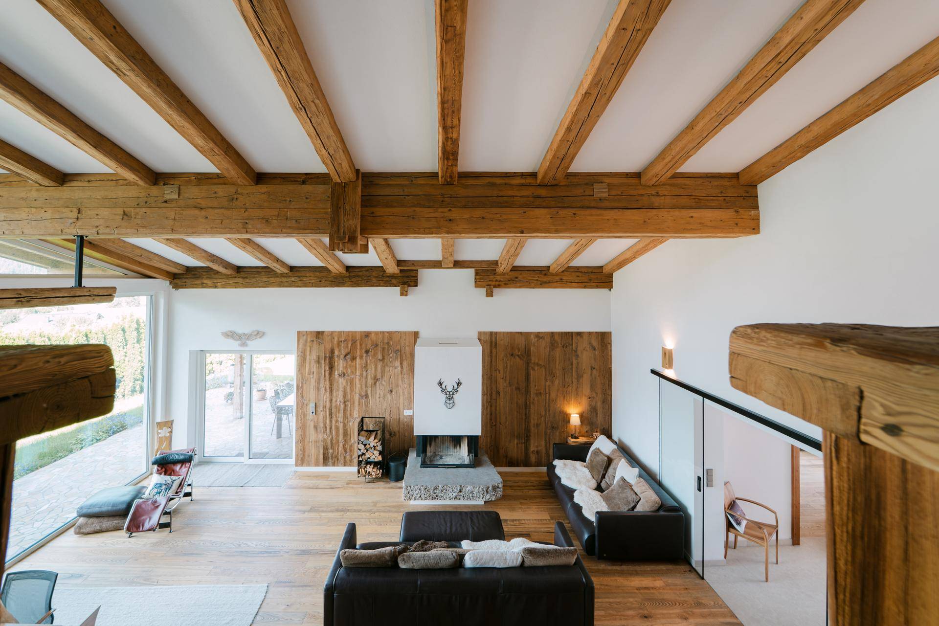 Gemütliches Wohnzimmer mit Kamin, Holzwänden und hohen Decken, die viel Licht hereinlassen.