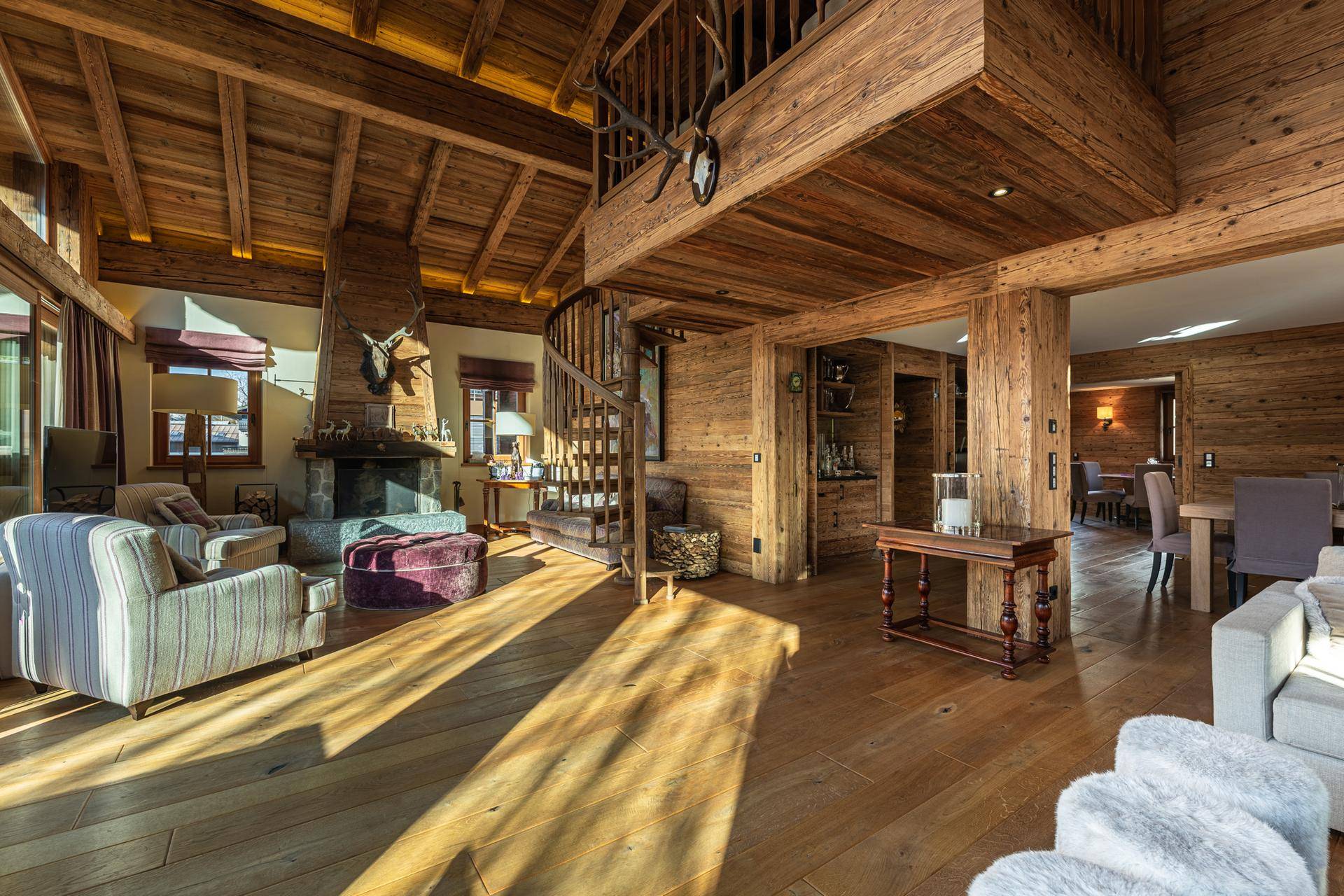 Großzügiges Wohnzimmer im alpinen Stil mit Kamin, hohen Decken und sichtbaren Holzbalken.