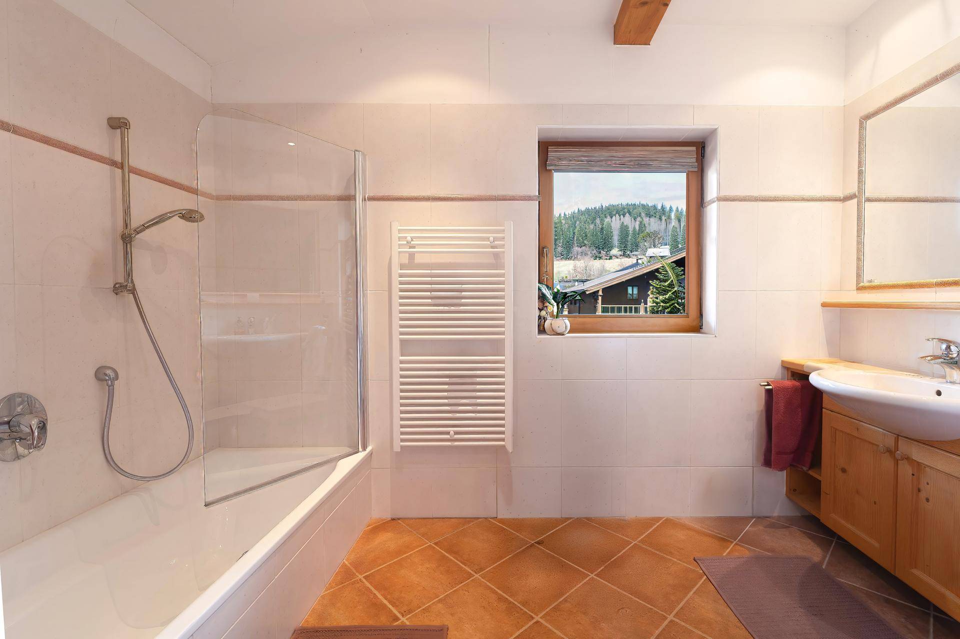 Helles Badezimmer mit Badewanne, Dusche, beheiztem Handtuchhalter und Fenster mit Ausblick.