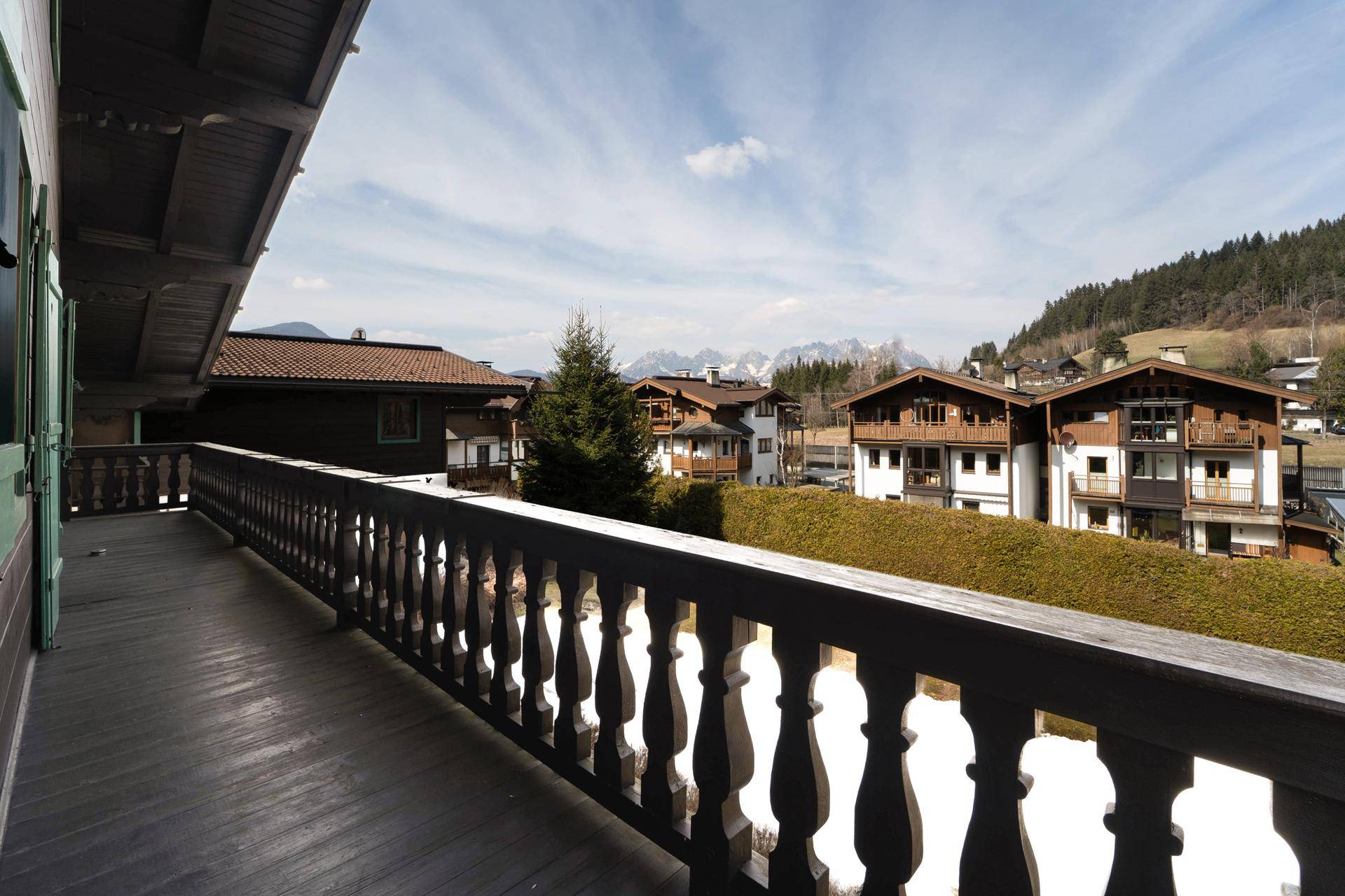 Geräumiger Holzbalkon mit traditionellem Geländer und Blick auf die umliegenden Häuser und Berge.