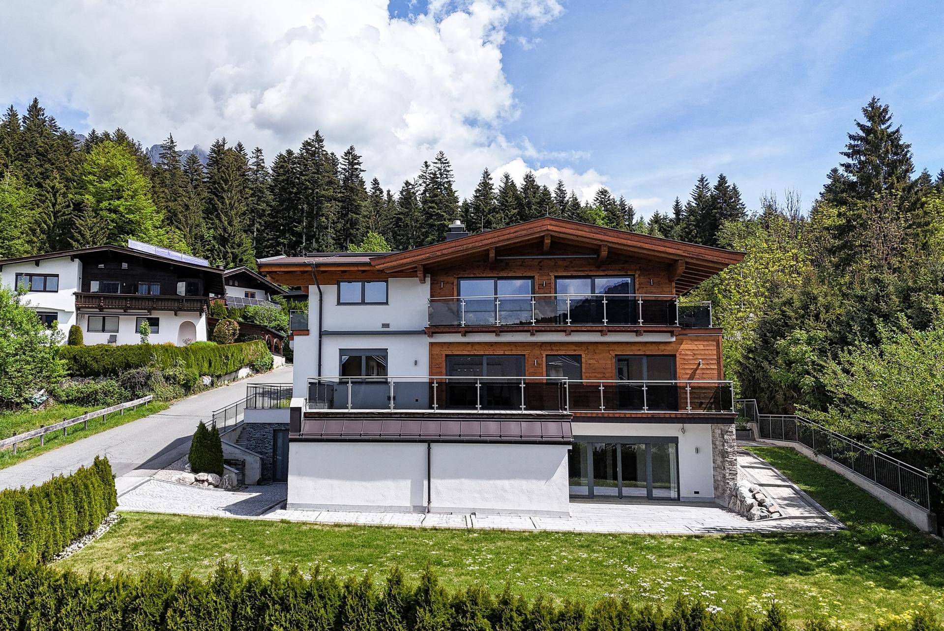 Attraktives Neubauhaus mit Holzverkleidung, großzügigen Balkonen und weitläufiger Rasenfläche.
