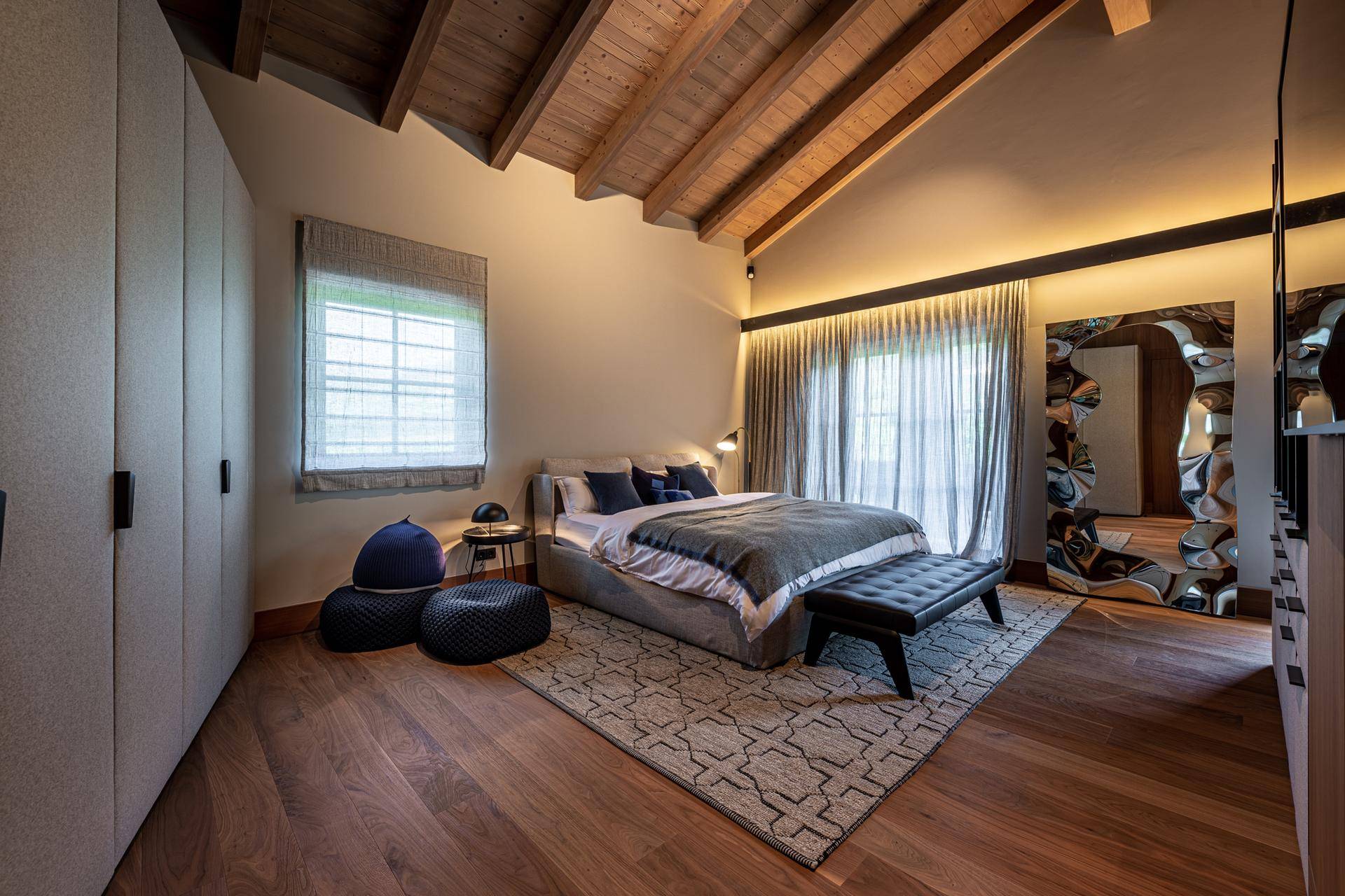 Helles Schlafzimmer mit Holzbalkendecke, großem Bett und Zugang zu einem Balkon.
