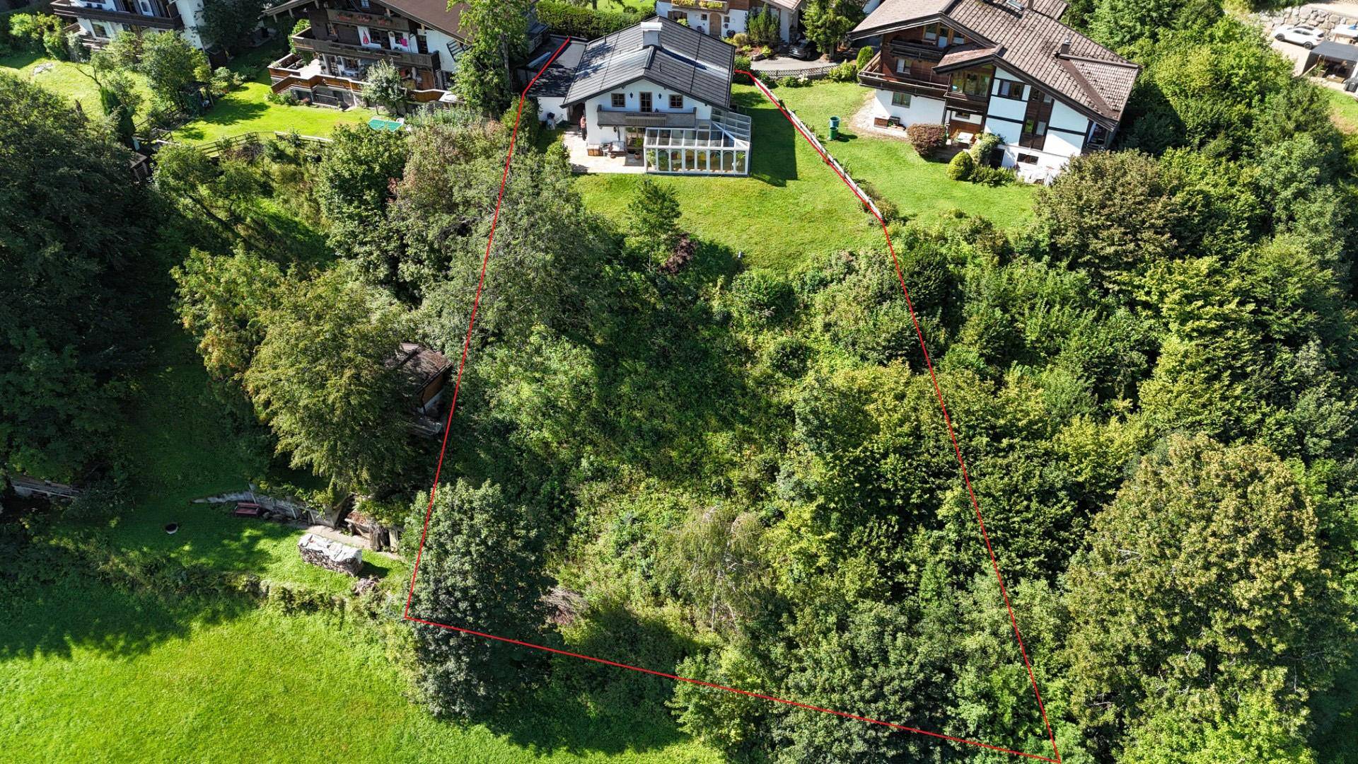 Luftaufnahme eines Hauses mit Wintergarten, umgeben von einem großen, grünen Grundstück mit Baumbestand.