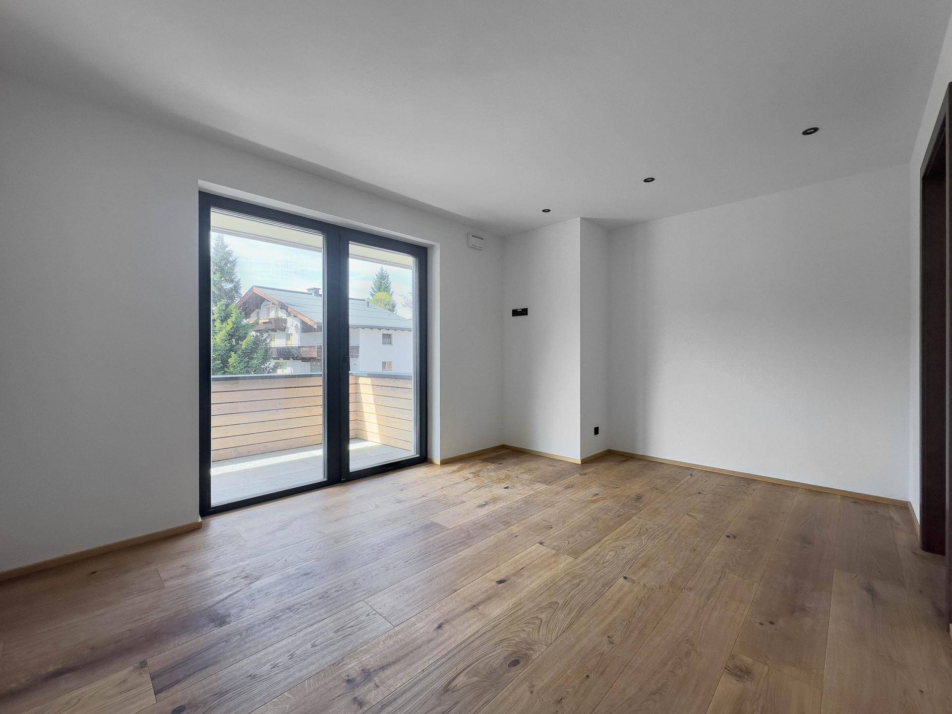Helles Zimmer mit Holzboden und großem Fenster, das Zugang zu einem Balkon bietet.