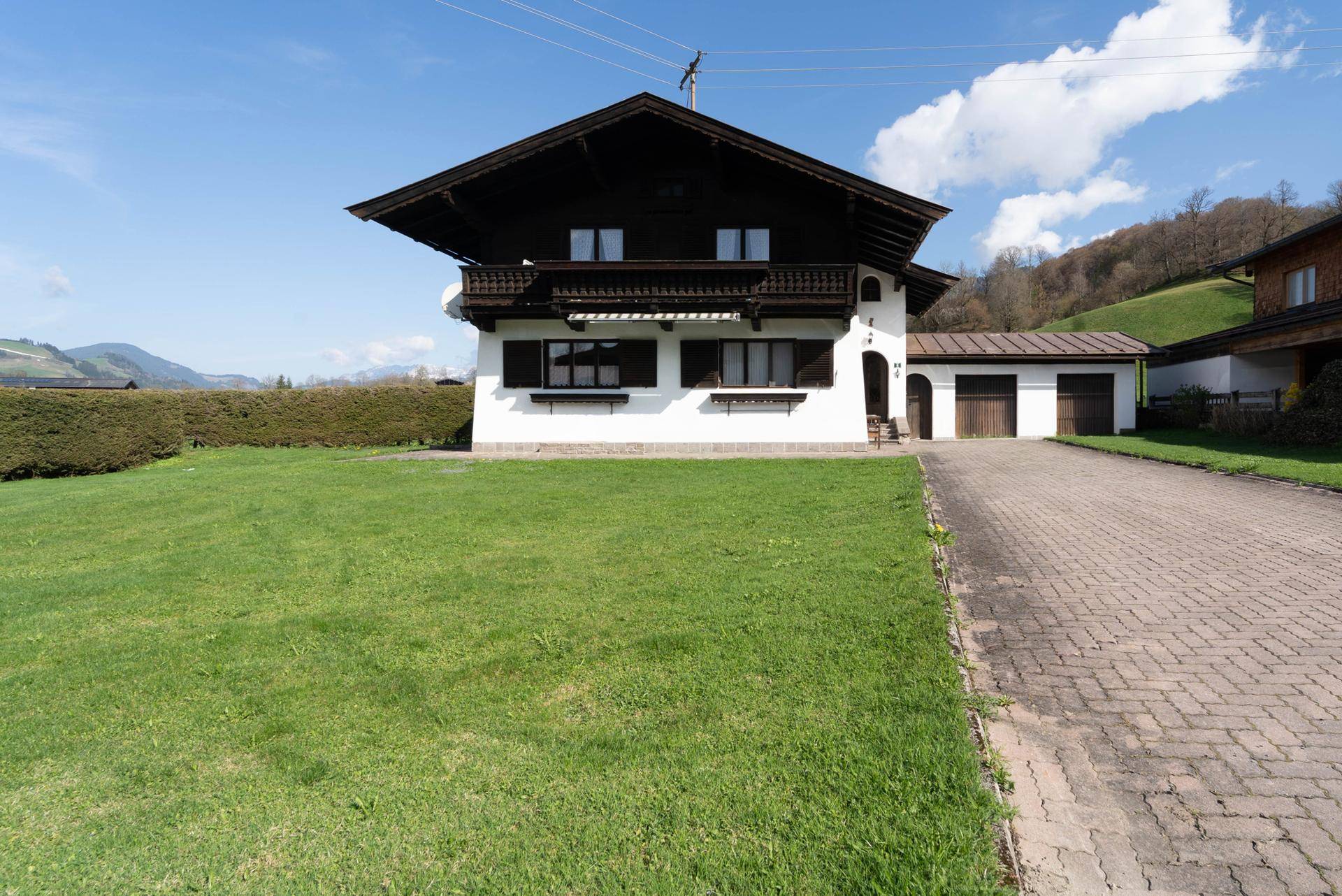 Vorderansicht des traditionellen Hauses mit gepflegtem Rasen, Auffahrt und Bergblick.