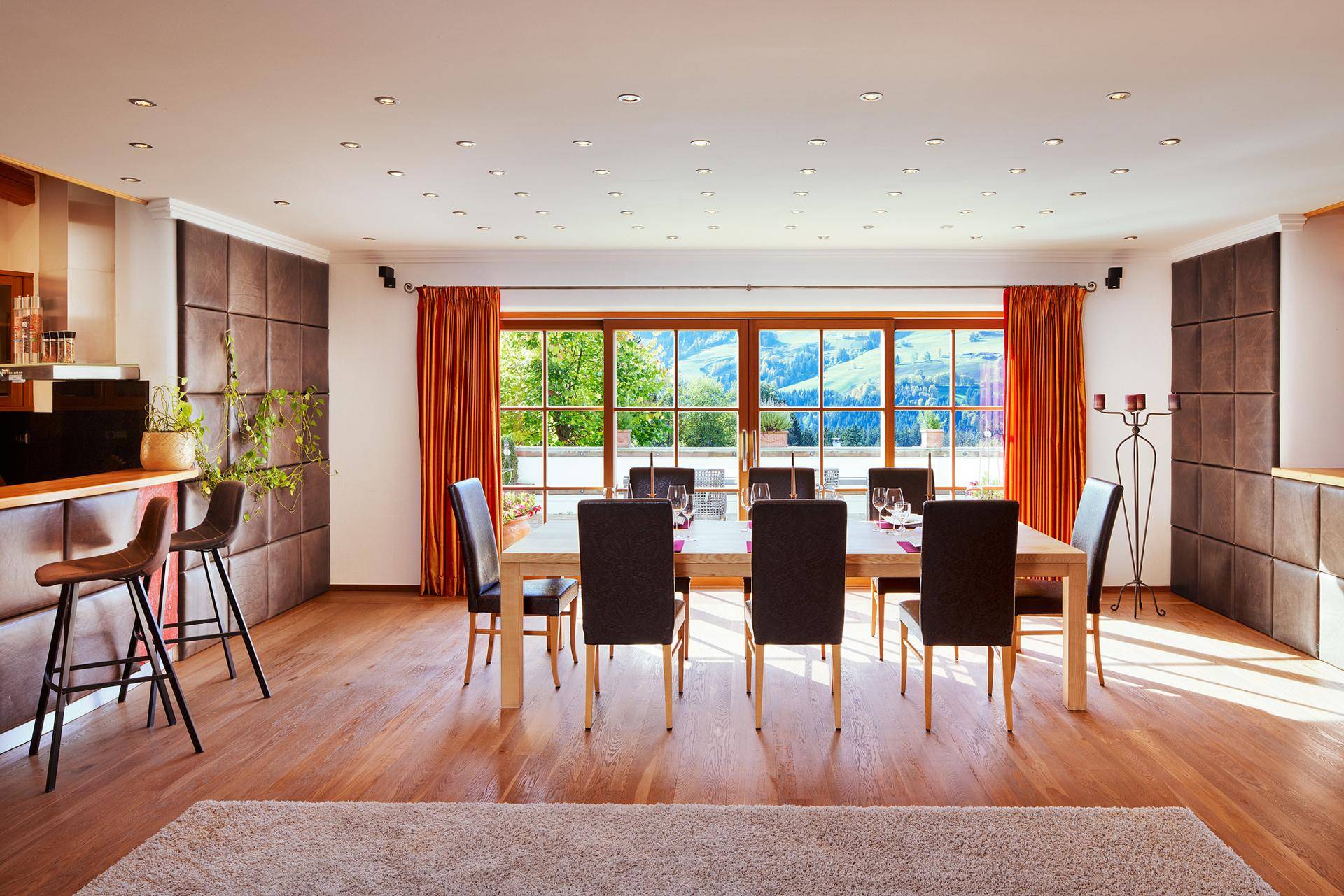 Heller Essbereich mit Holzboden, großem Tisch und Panoramablick auf die Berge durch die Fensterfront.