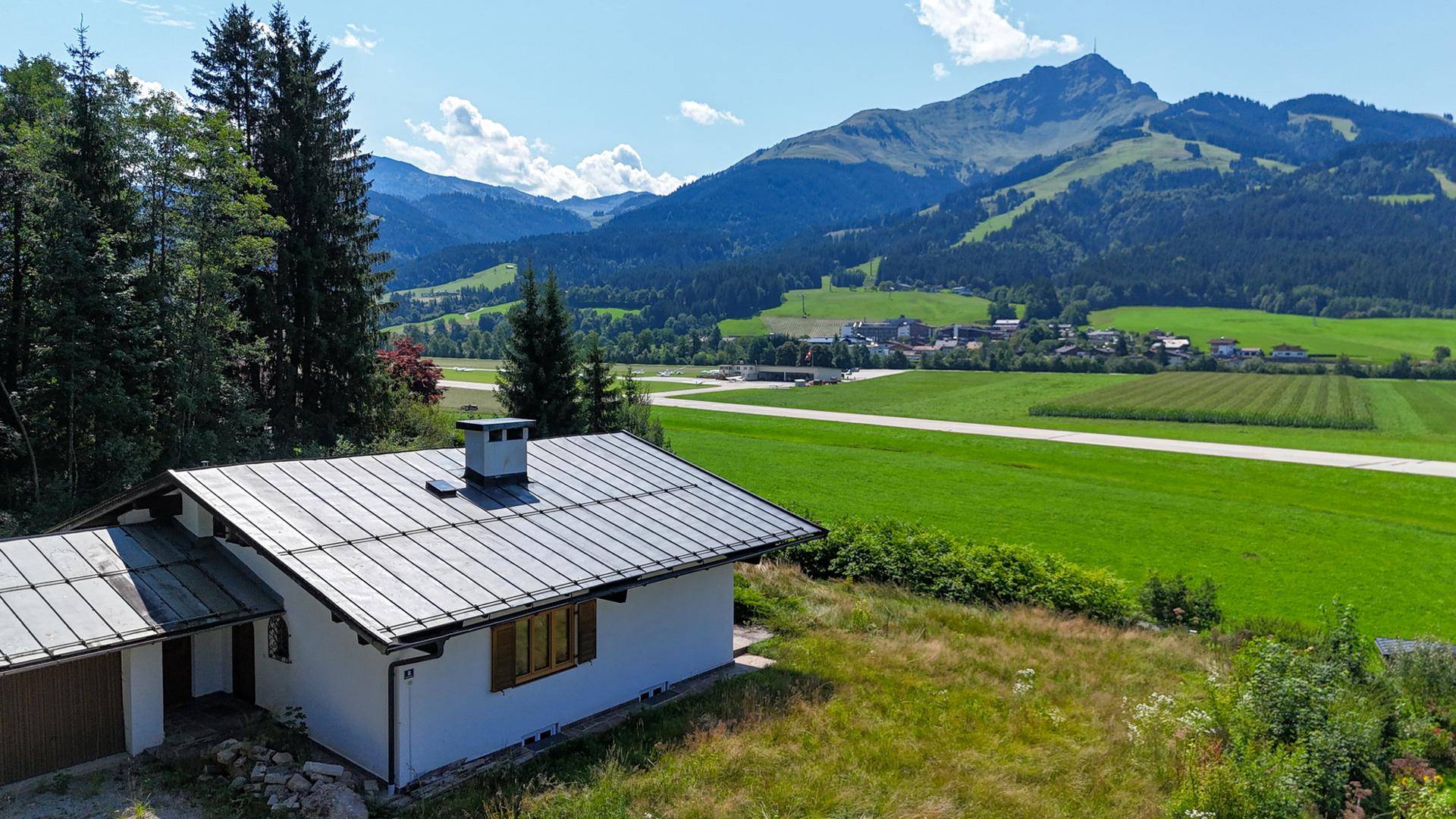 Einfamilienhaus mit Metall-Satteldach, umgeben von Natur und Bergblick in der Ferne.