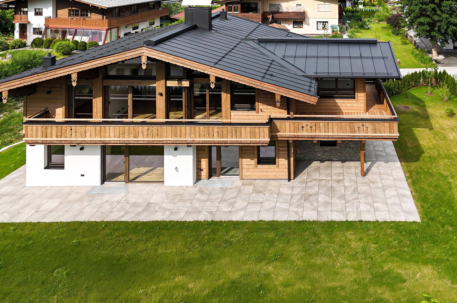 Vogelperspektive eines modernen Holzchalets mit dunklem Satteldach und großzügiger Terrasse.