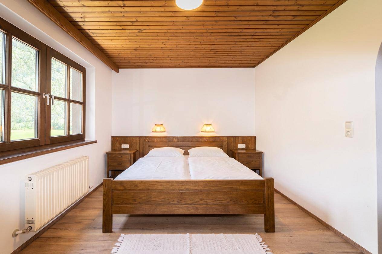 Schlafzimmer mit Doppelbett, Holzmöbeln und Fenster mit Blick ins Grüne.