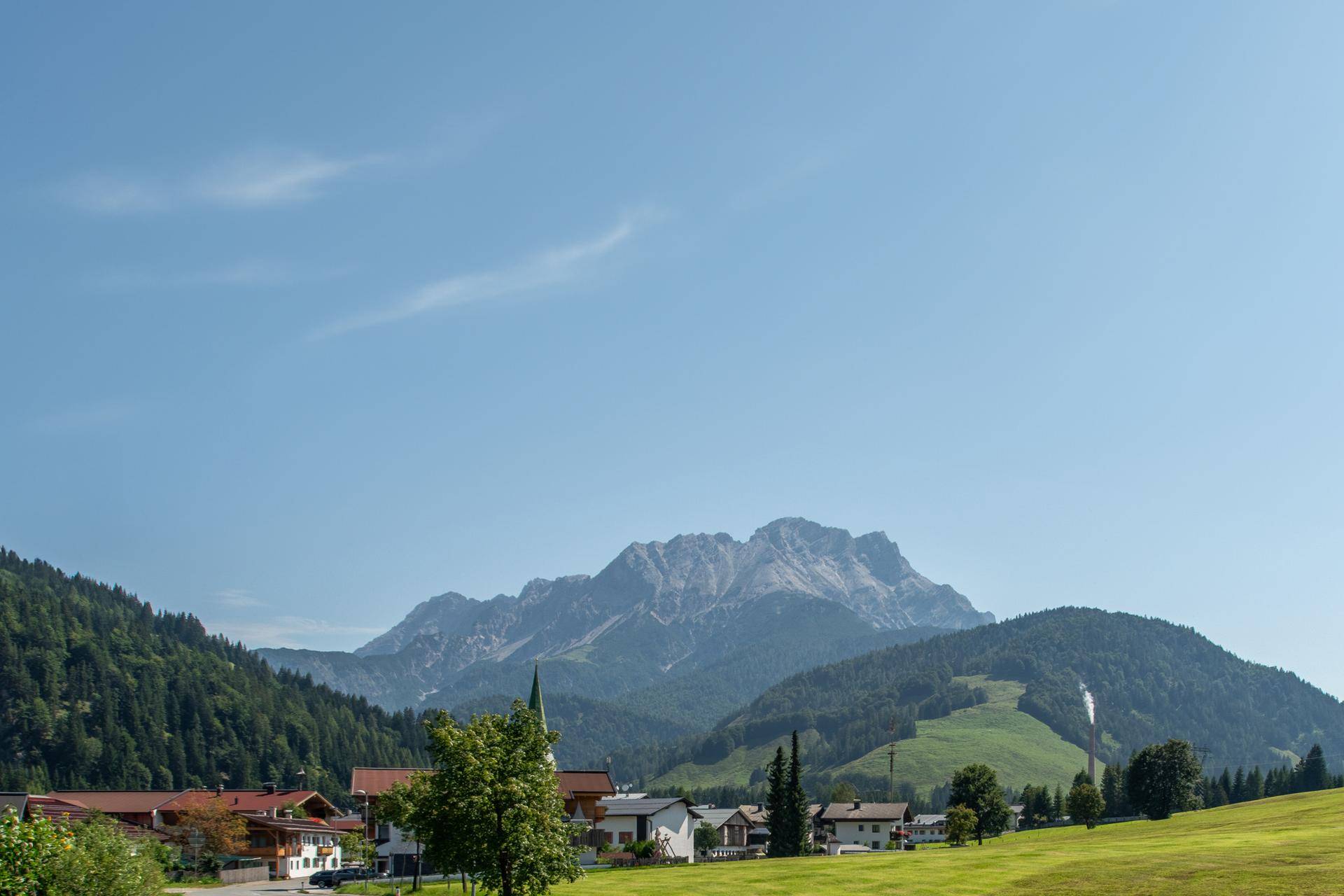 Malerische Landschaft mit majestätischen Bergen, grünen Hügeln und einem charmanten Dorf unter klarem Himmel.