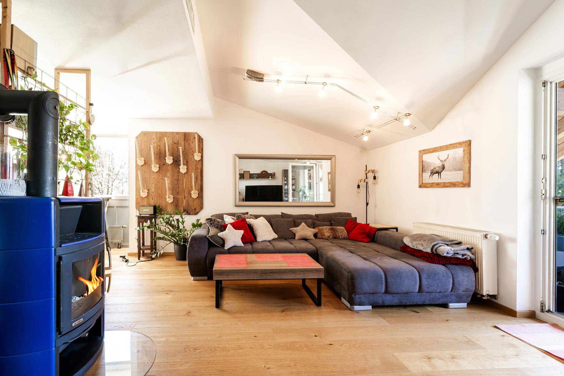 Gemütliches Wohnzimmer mit Holzboden, modernem Kaminofen und großem Sofa unter der Dachschräge.