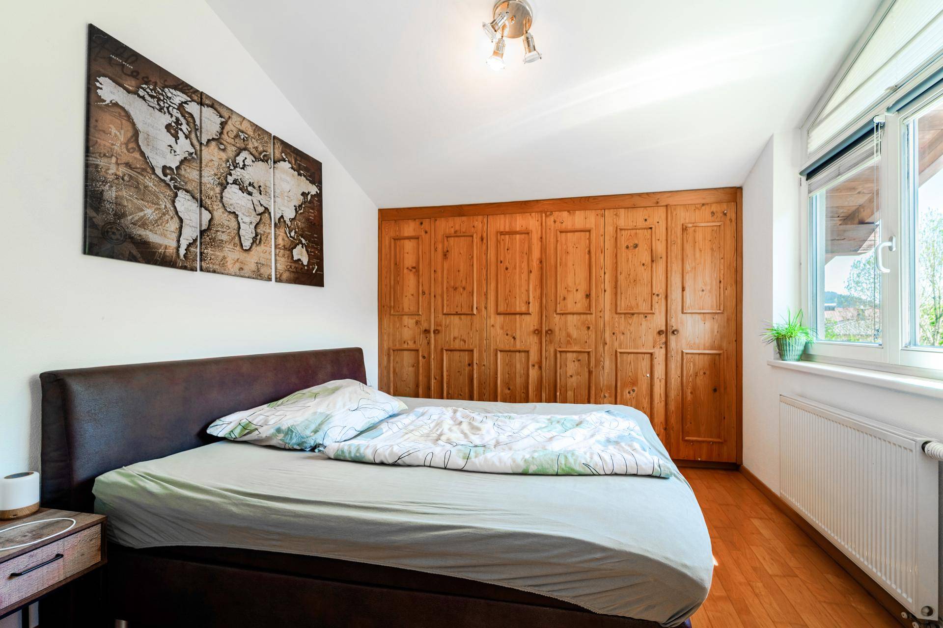 Schlafzimmer mit Holzboden, integrierten Holzschränken und einem Fenster unter der Dachschräge.