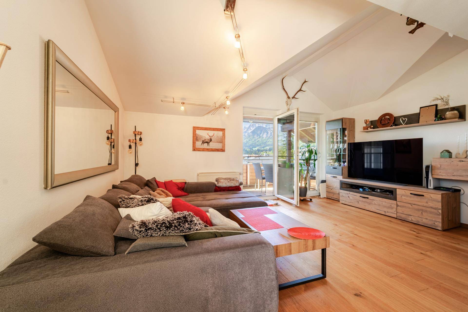 Helles Wohnzimmer mit Zugang zum Balkon, TV-Möbeln und Blick auf die umliegende Berglandschaft.