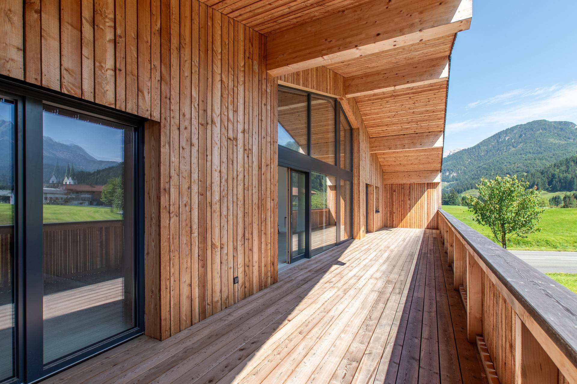 Langer Holzbalkon mit Holzfassade und weitem Blick auf die umliegende Berglandschaft.