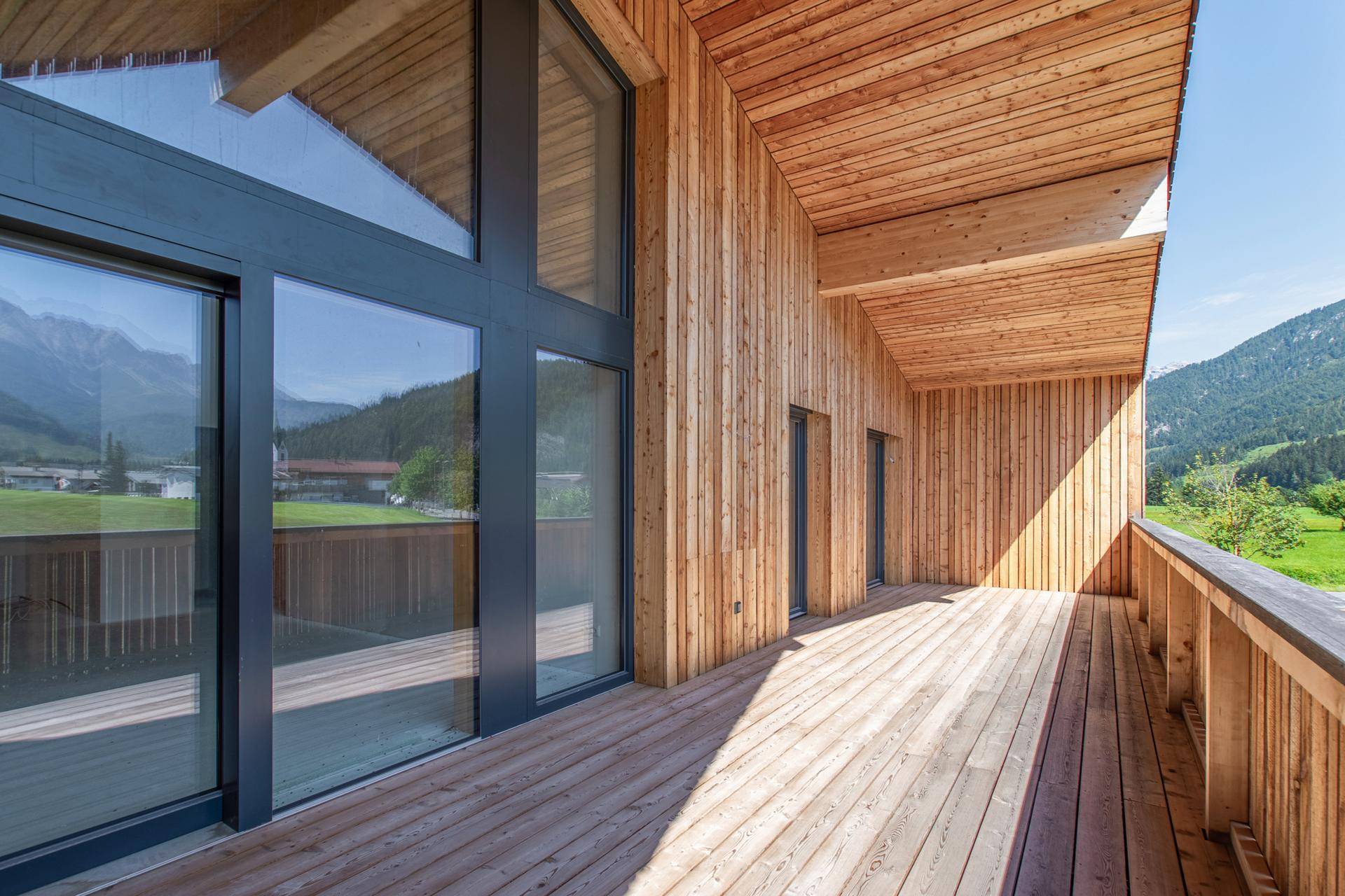 Moderner Holzbalkon mit großen Fenstern und weitem Blick auf die grüne Landschaft.