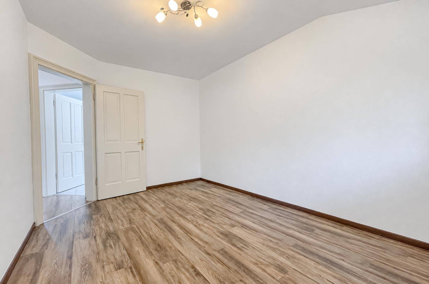 Leeres Zimmer mit Laminatboden und weißen Wänden, bereit zur individuellen Gestaltung.