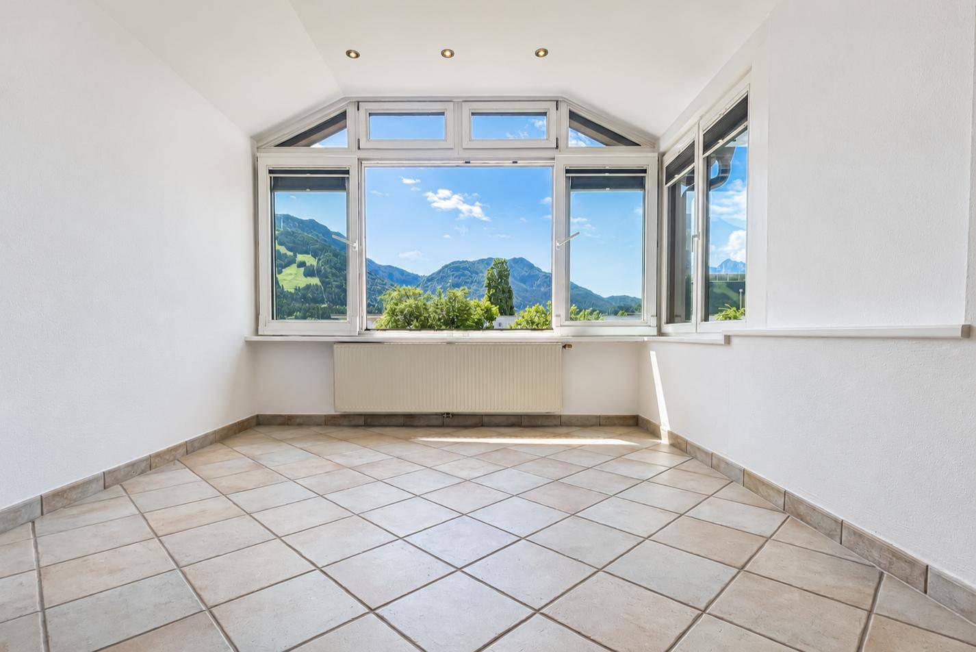 Heller Wintergarten mit Fliesenboden und weitem Blick auf die umliegende Berglandschaft.