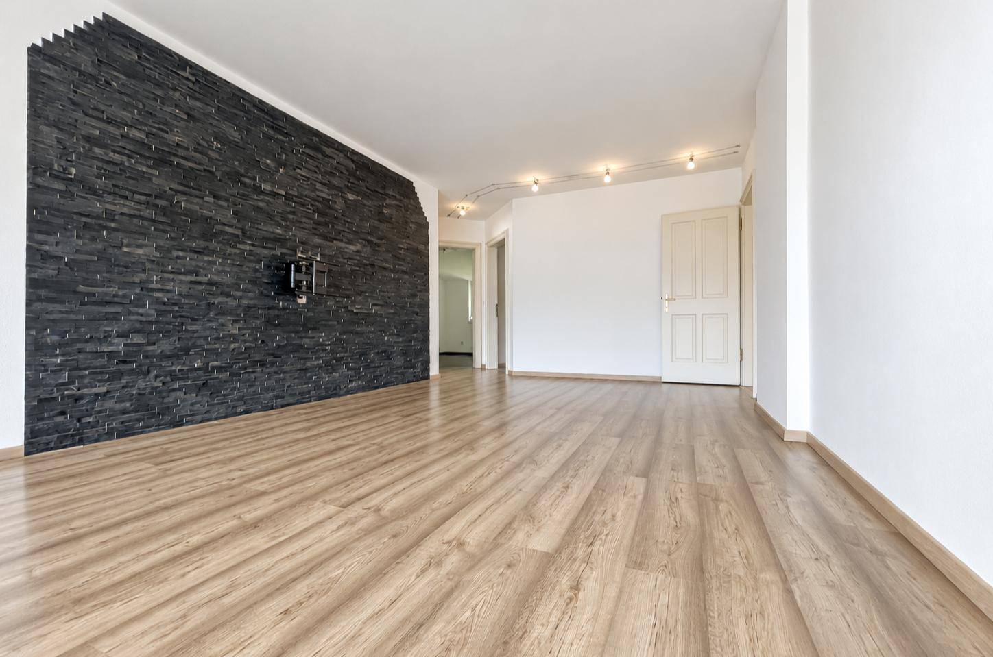 Geräumiges Wohnzimmer mit Laminatboden und einer markanten Schieferwand als Akzent.