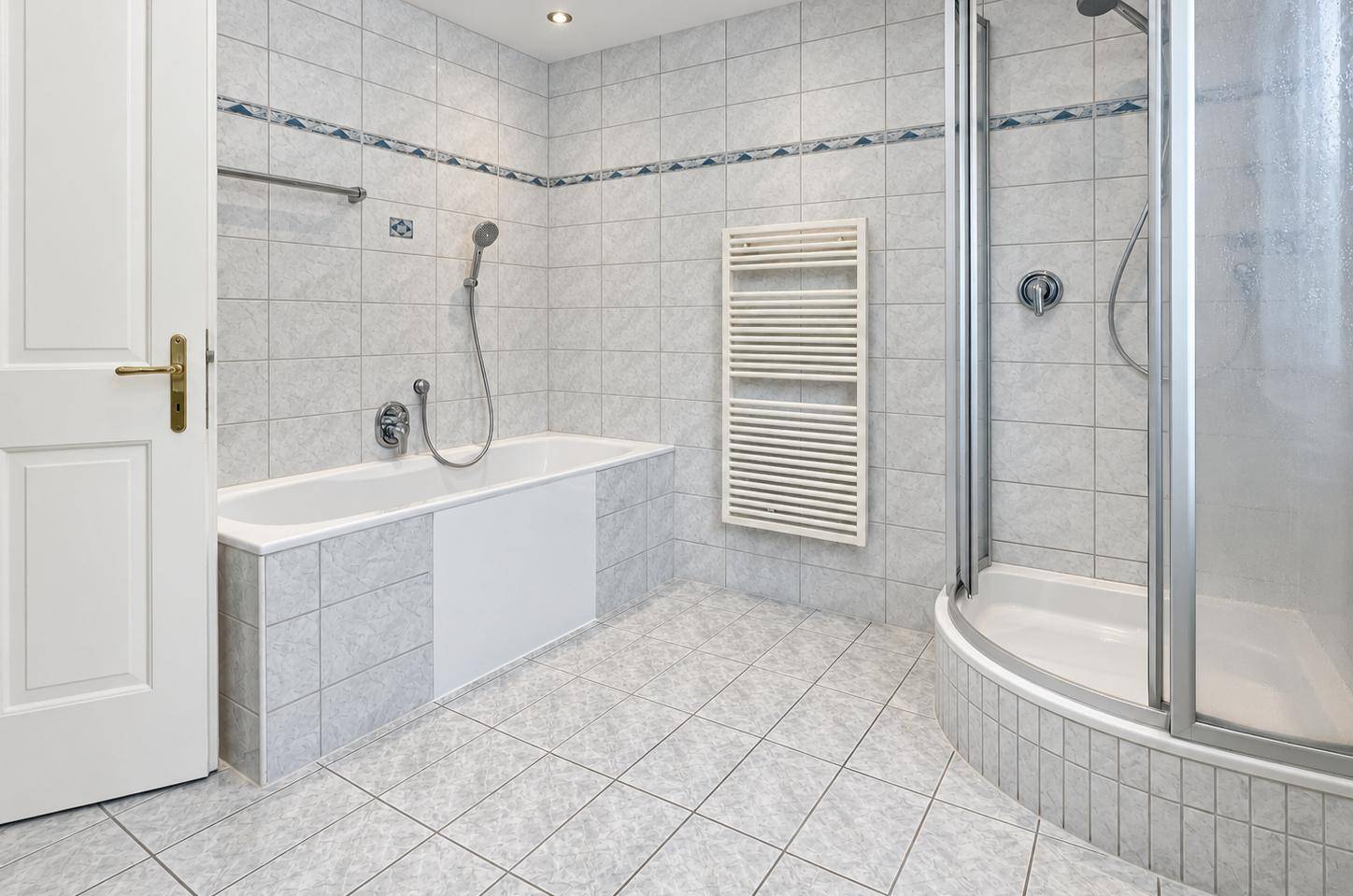 Helles Badezimmer mit hellgrauen Fliesen, Badewanne, Duschkabine und Handtuchheizkörper.