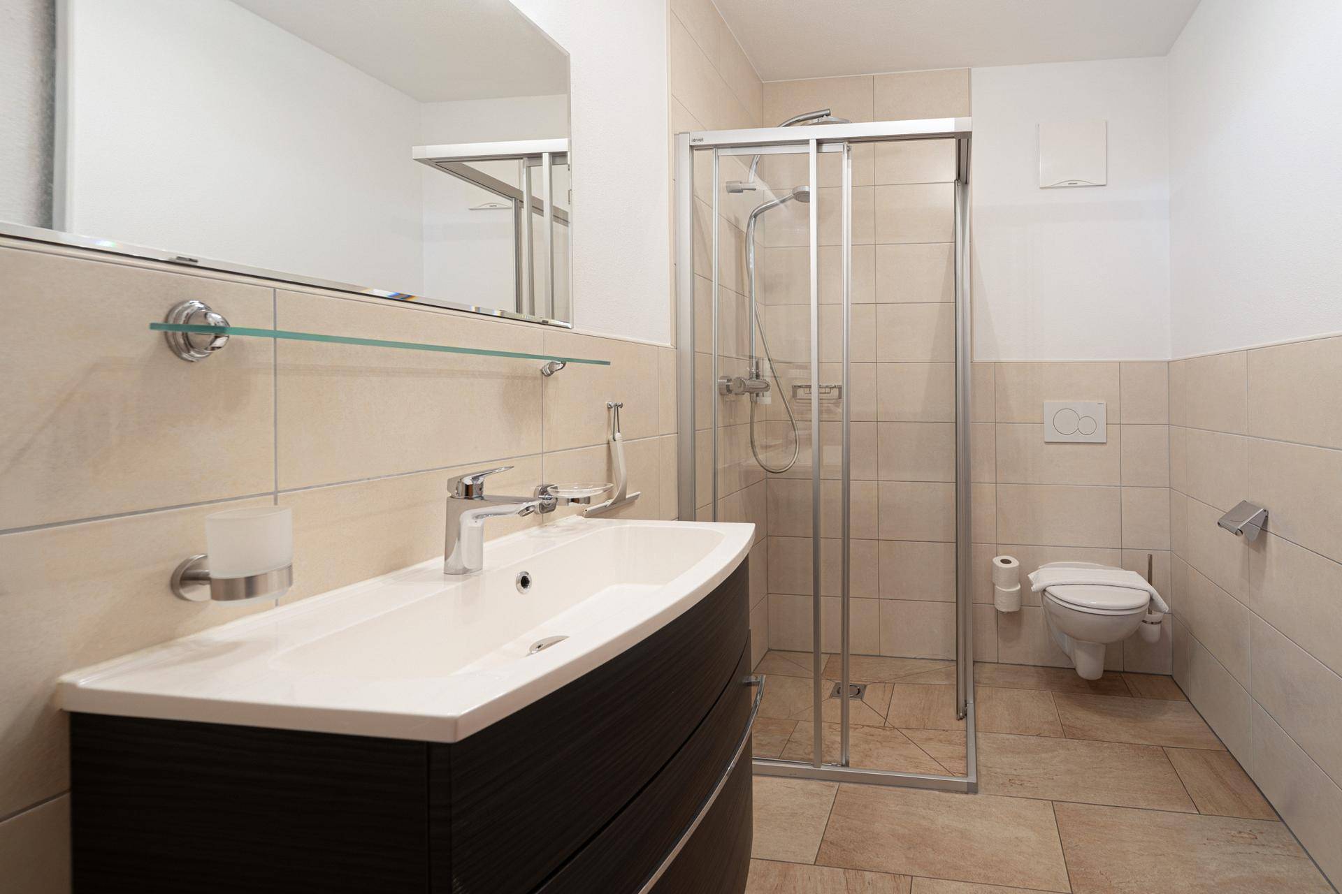 Helles Badezimmer mit modernem Waschtisch, Duschkabine und wandhängendem WC.