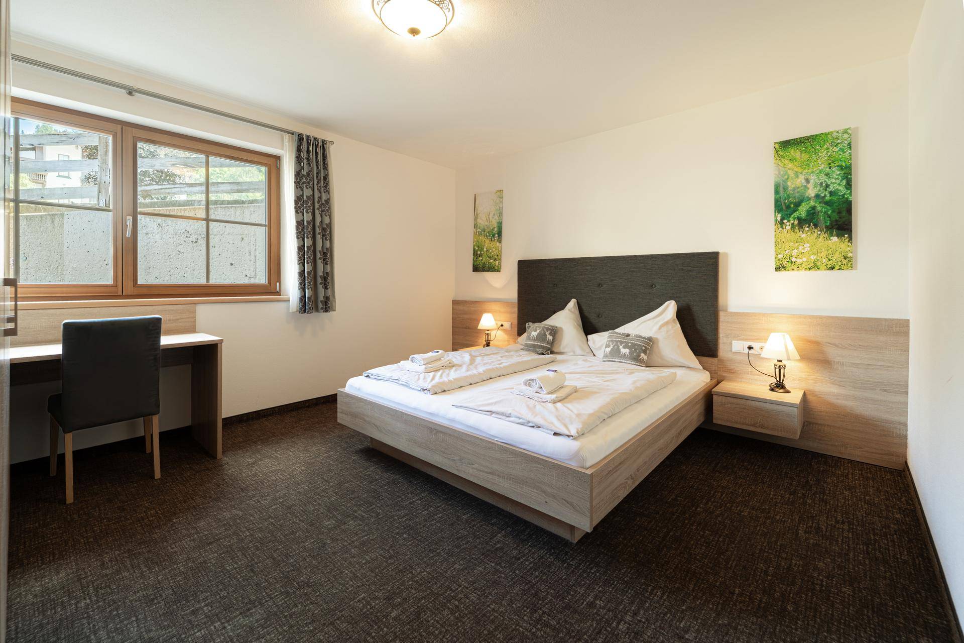 Gemütliches Schlafzimmer mit Doppelbett, Holzelementen und einem Schreibtisch am Fenster.