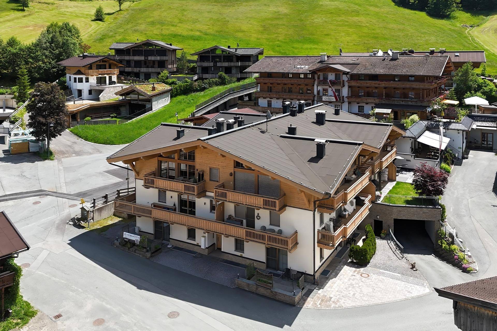Luftaufnahme eines modernen Gebäudes mit Holzfassade und Balkonen in alpiner Umgebung.