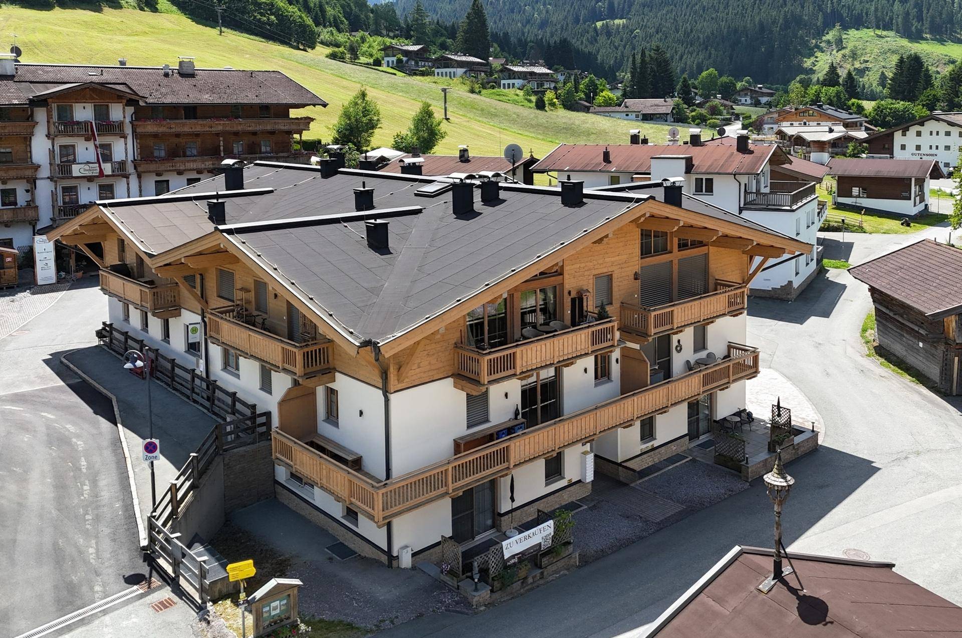 Attraktives Mehrfamilienhaus im alpinen Stil mit Holzfassade und Balkonen in grüner Umgebung.
