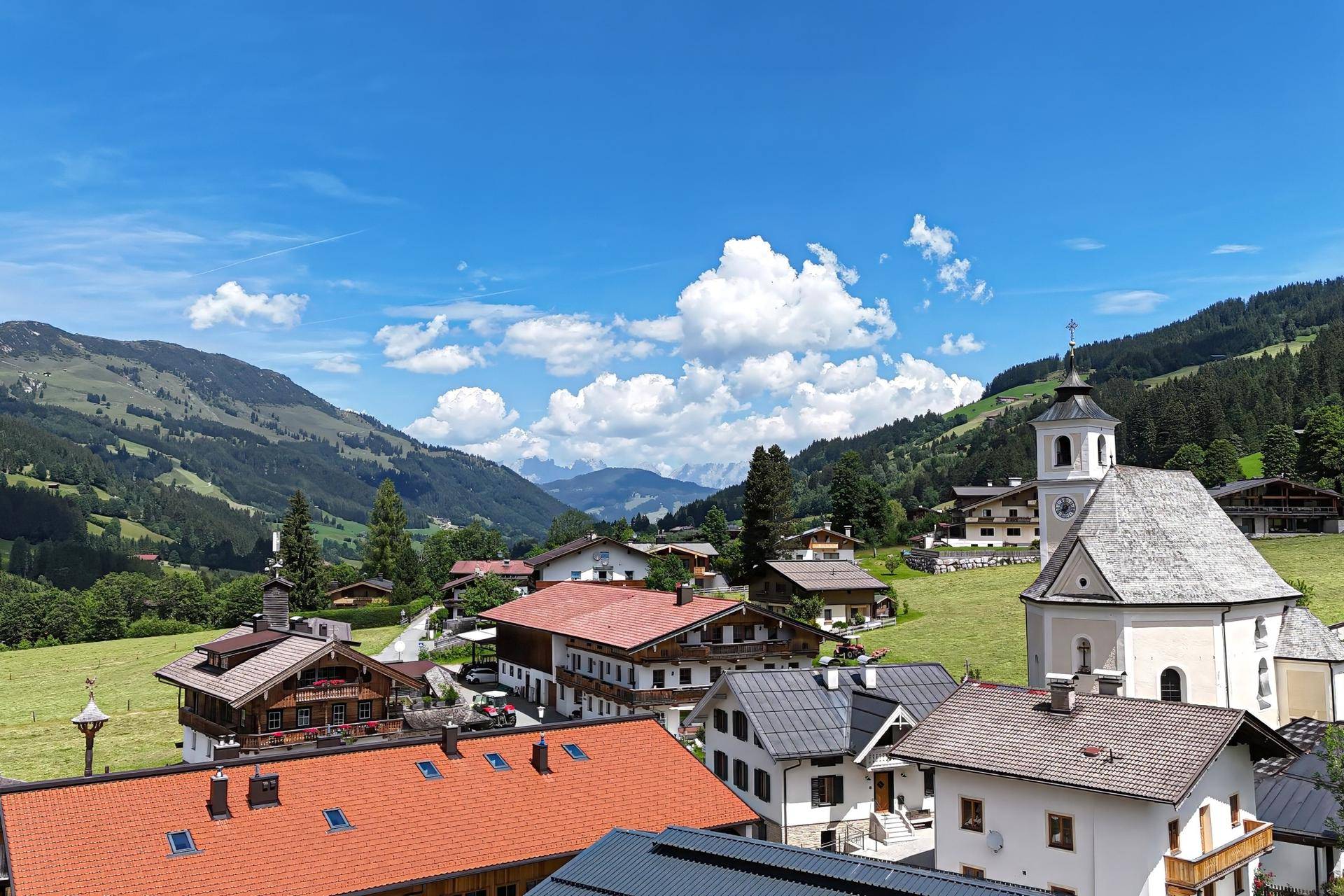 Malerische Berglandschaft mit traditionellen Häusern und einer Kirche unter blauem Himmel.