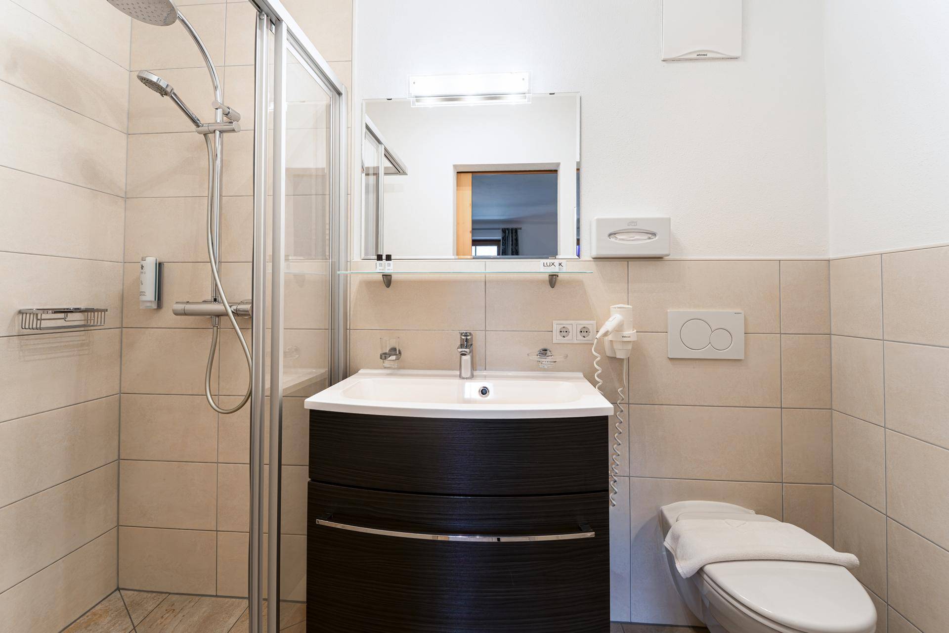 Modernes Badezimmer mit Duschkabine, Waschbecken und Wand-WC in hellen Fliesen.