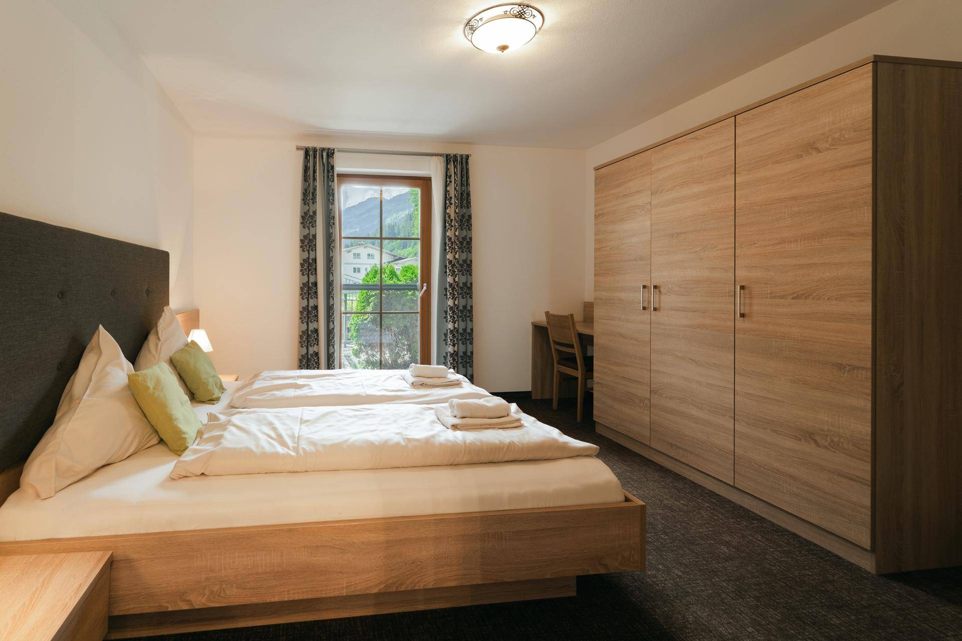 Gemütliches Schlafzimmer mit Doppelbett, Holzmöbeln und Blick auf die Berge.
