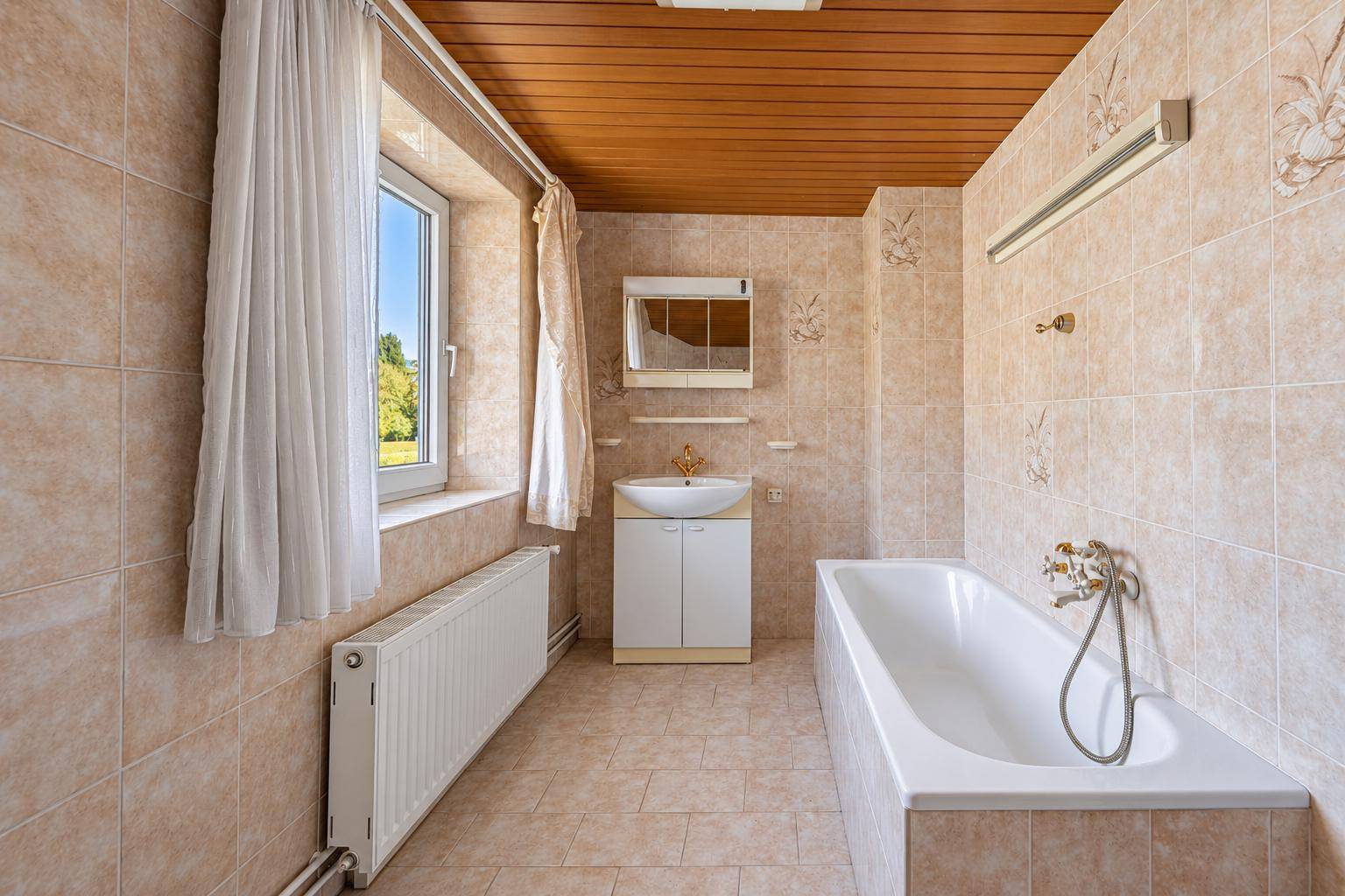 Badezimmer mit Badewanne, Fliesenboden und Fenster für Tageslicht.