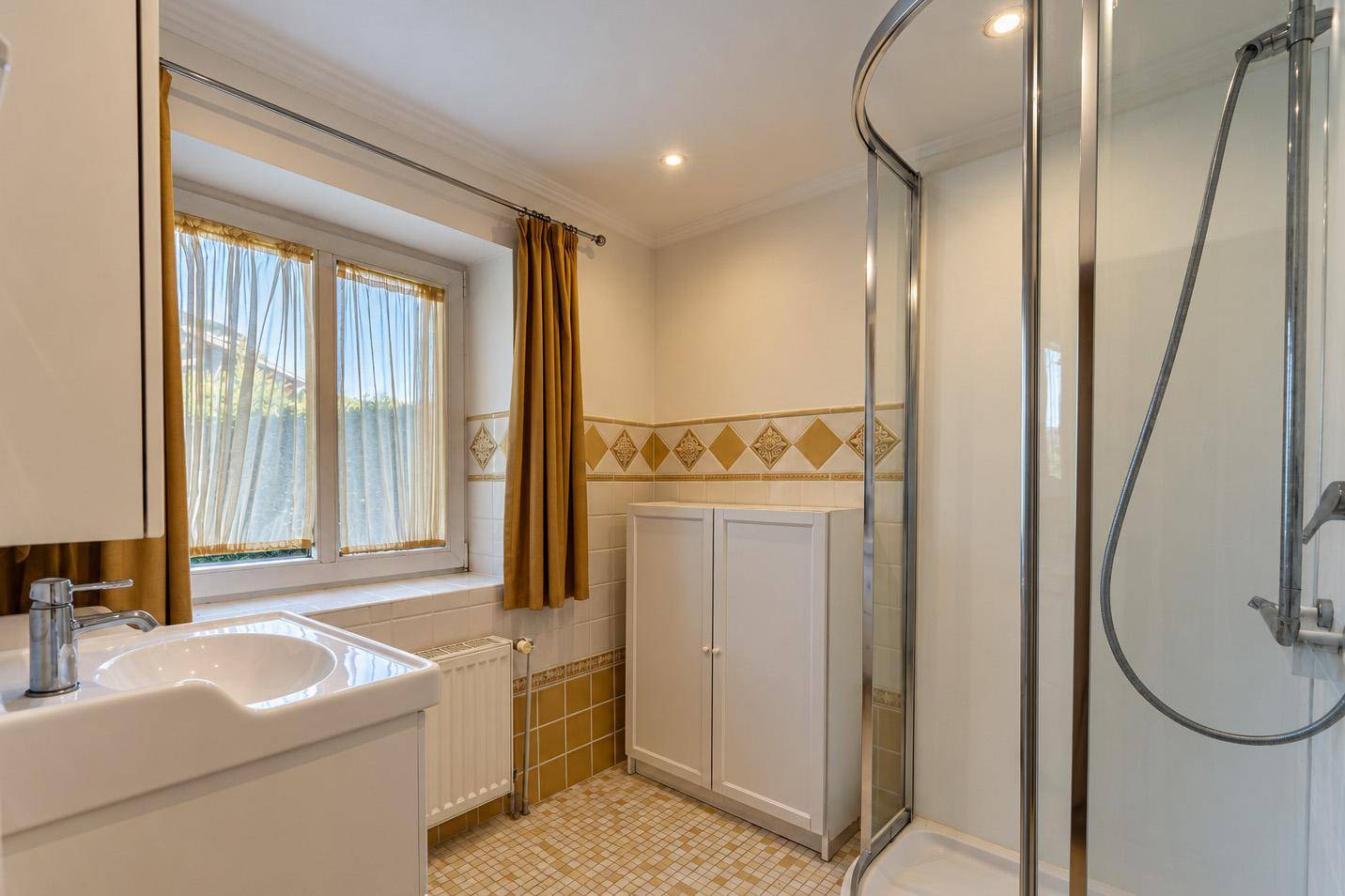 Badezimmer mit Duschkabine, Fenster und gemusterten Fliesen.