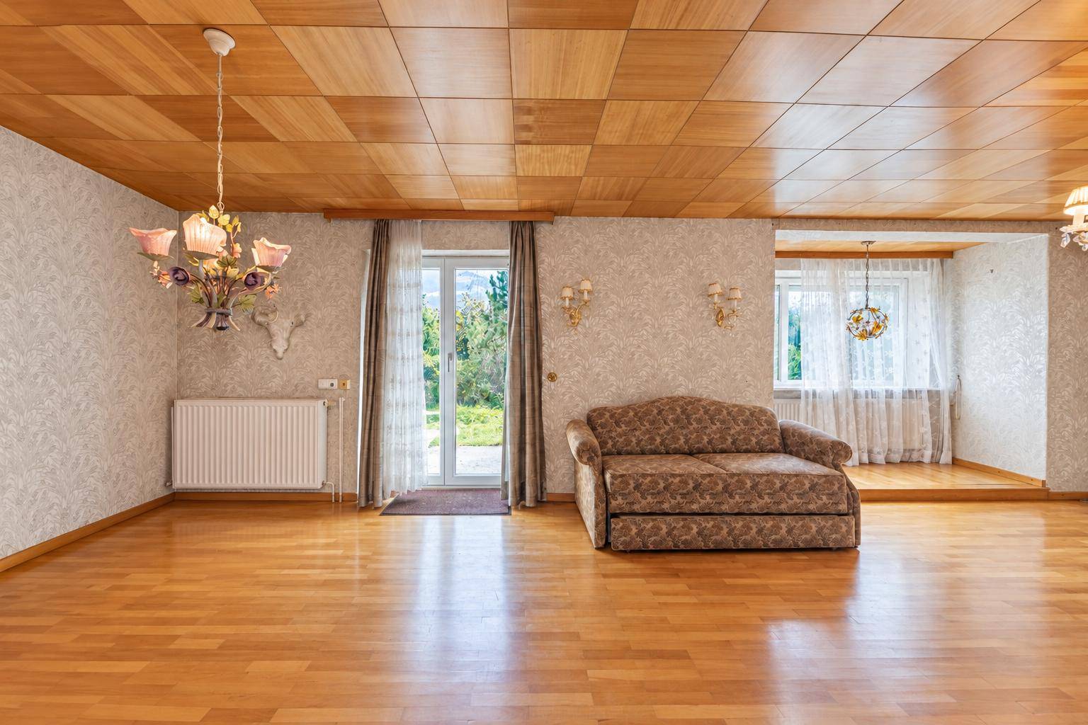 Geräumiges Wohnzimmer mit Holzdecken, Parkettboden und Zugang zum Garten.