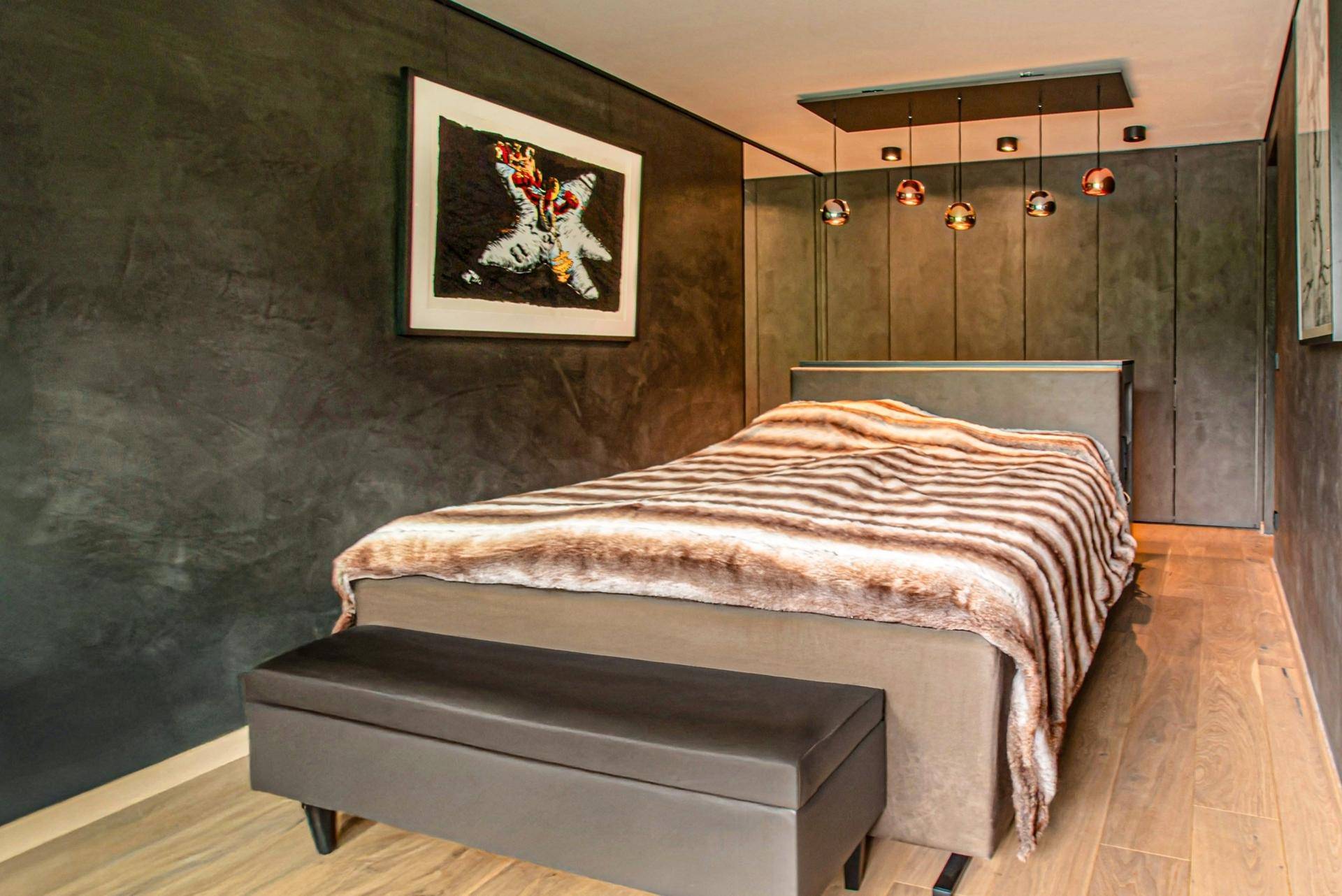 Modernes Schlafzimmer mit dunklen Wänden, Holzboden und stilvoller Beleuchtung, die eine gemütliche Atmosphäre schafft.