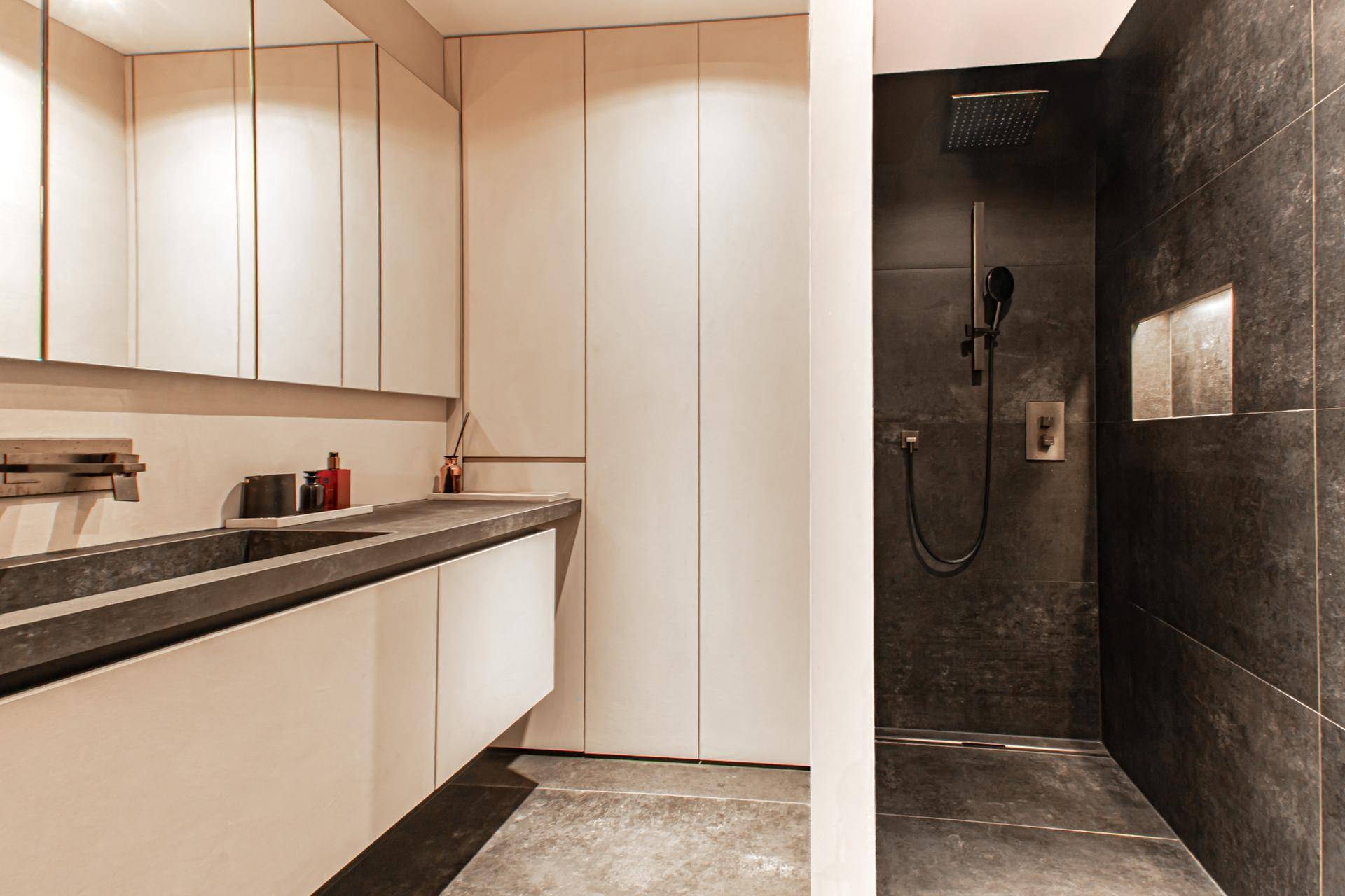 Modernes Badezimmer mit Doppelwaschbecken, begehbarer Dusche und dunklen Fliesen, die ein elegantes Ambiente schaffen.