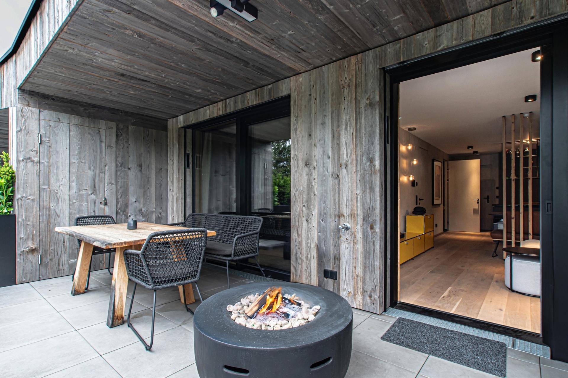 Gemütliche Terrasse mit Holzwänden, Außenmöbeln und einer Feuerstelle für entspannte Abende im Freien.