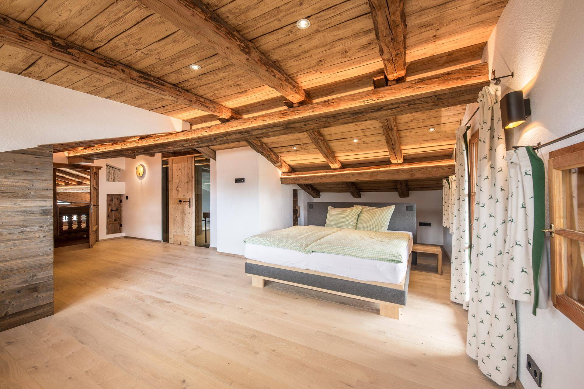 Helles Schlafzimmer mit Holzbalkendecke, Holzboden und modernem Bett im alpinen Stil.
