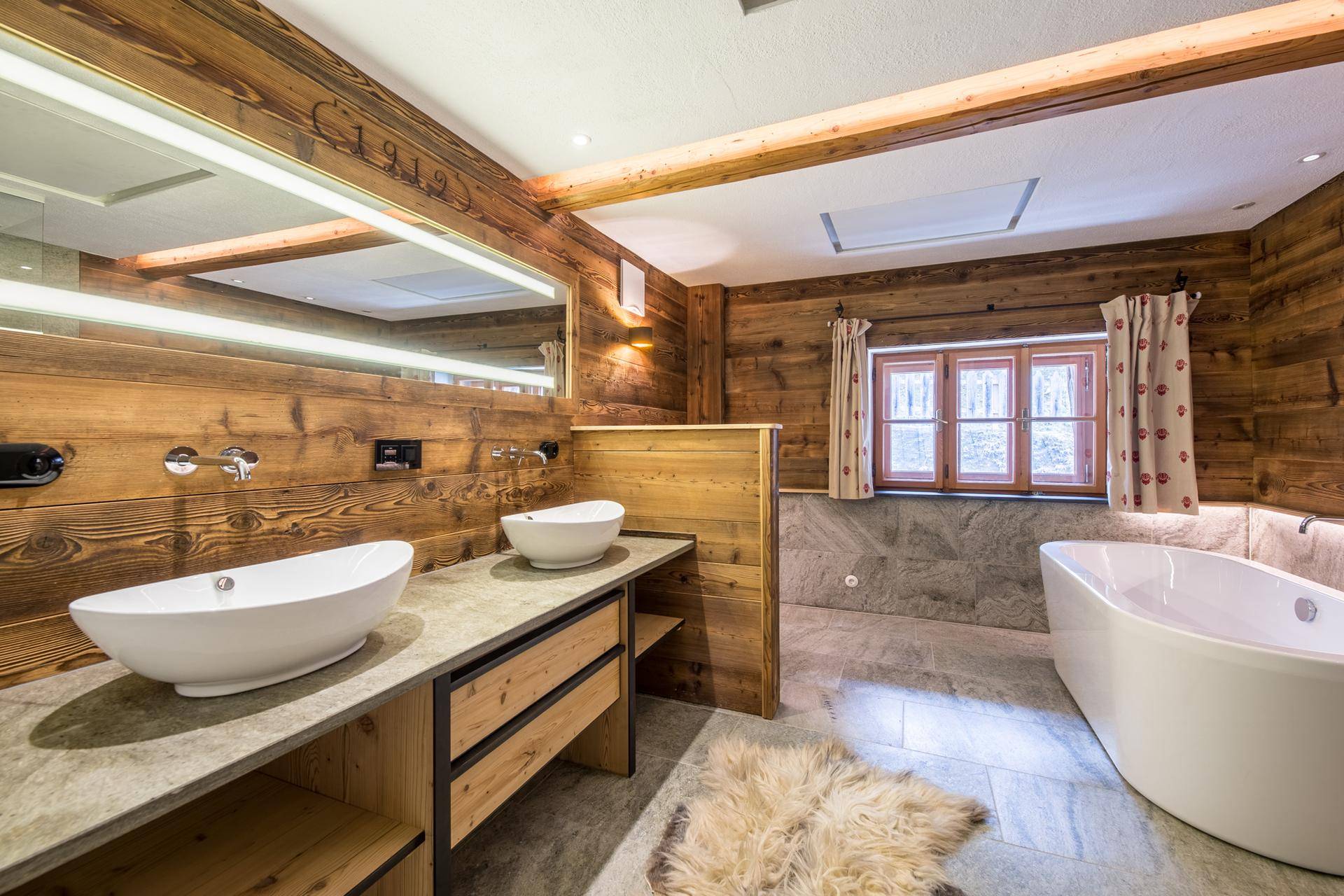 Modernes Badezimmer im Alpenstil mit Doppelwaschbecken, freistehender Badewanne und Holzverkleidung.