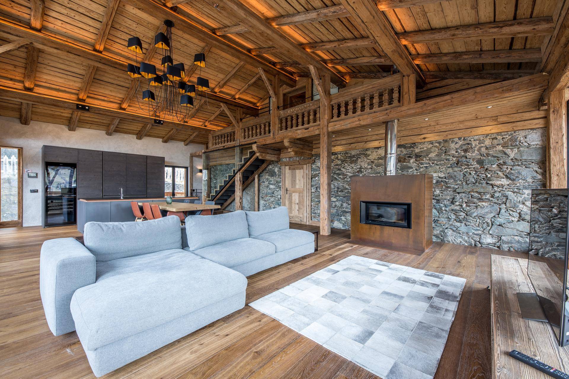 Geräumiges Wohnzimmer im Alpenstil mit Holzbalkendecke, Steinfassade und modernem Kamin.