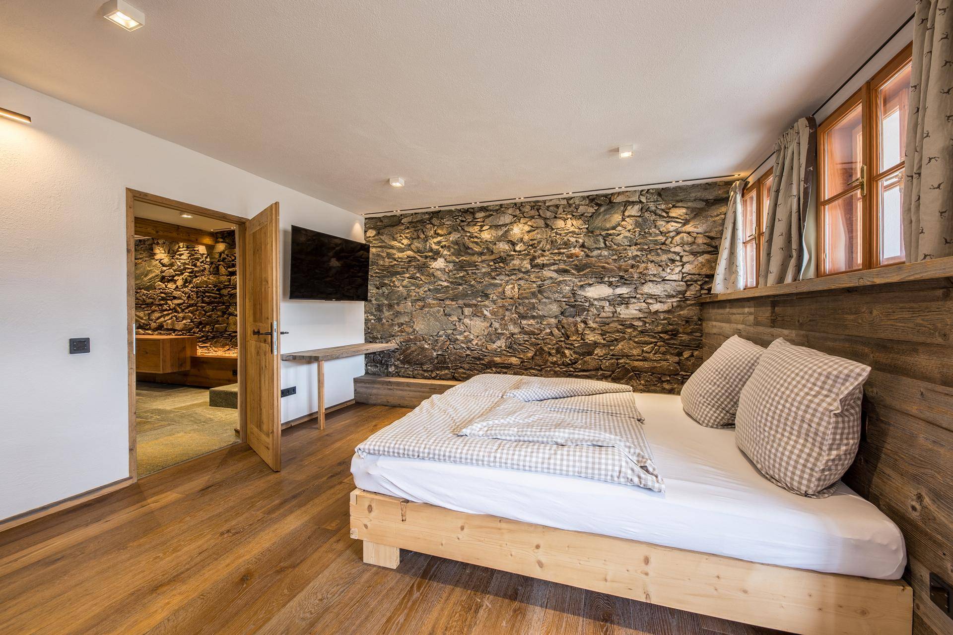 Schlafzimmer mit Holzboden, Steinwand und Zugang zu einem angrenzenden Wellnessbereich.