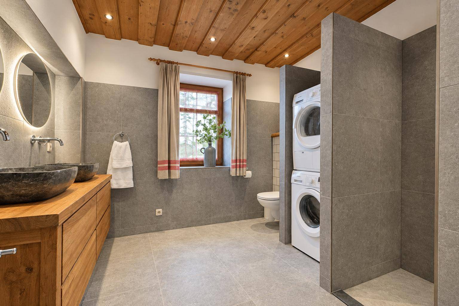 Modernes Badezimmer mit grauen Fliesen, Doppelwaschbecken und integrierter Waschmaschine.