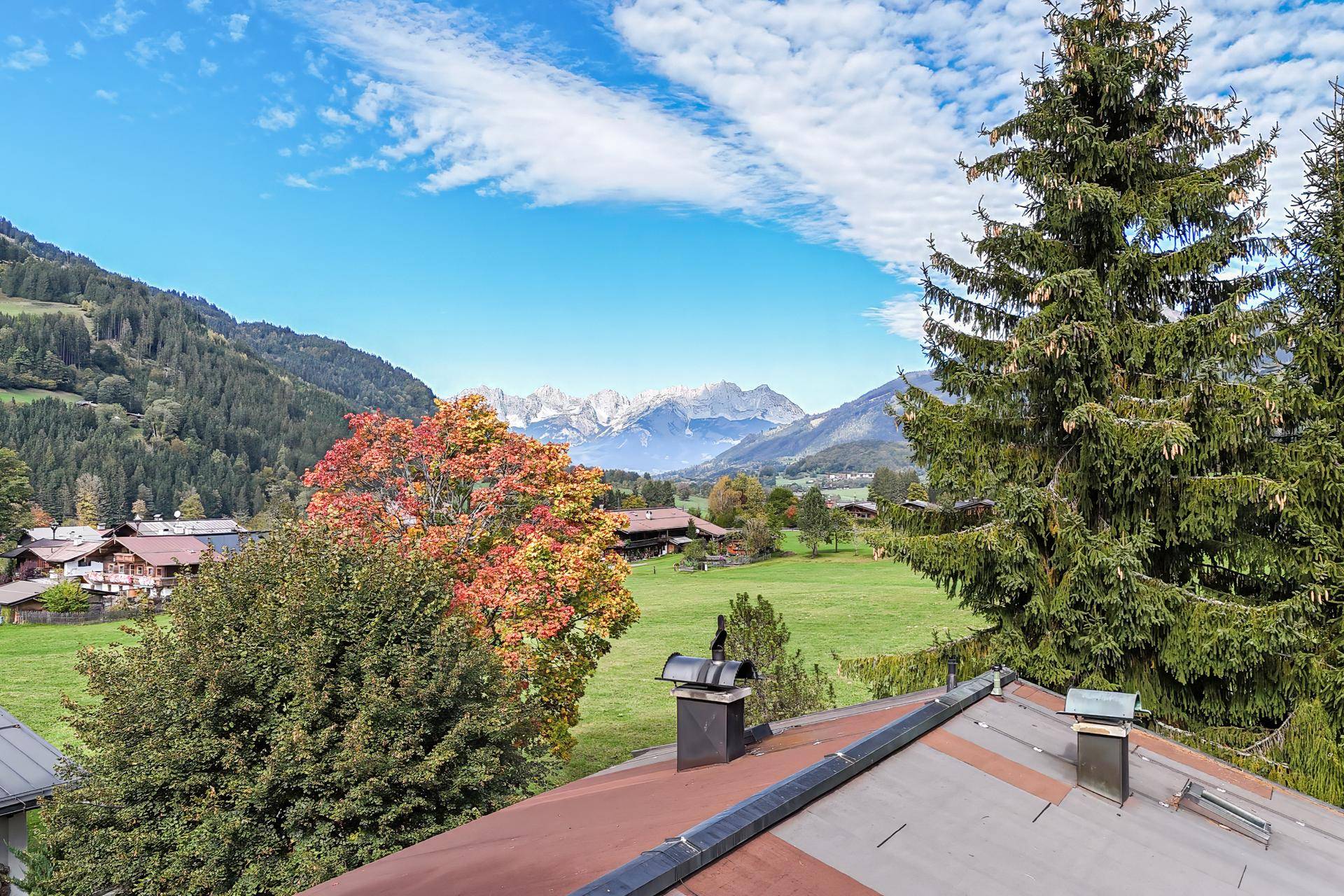 Malerischer Ausblick über grüne Wiesen und herbstliche Bäume auf die majestätischen Berge.