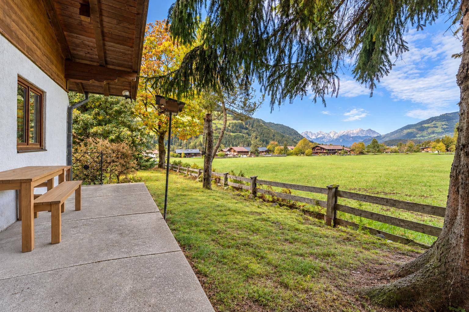 Einfache Terrasse mit Holztisch und Blick auf die weiten grünen Felder und Berge.
