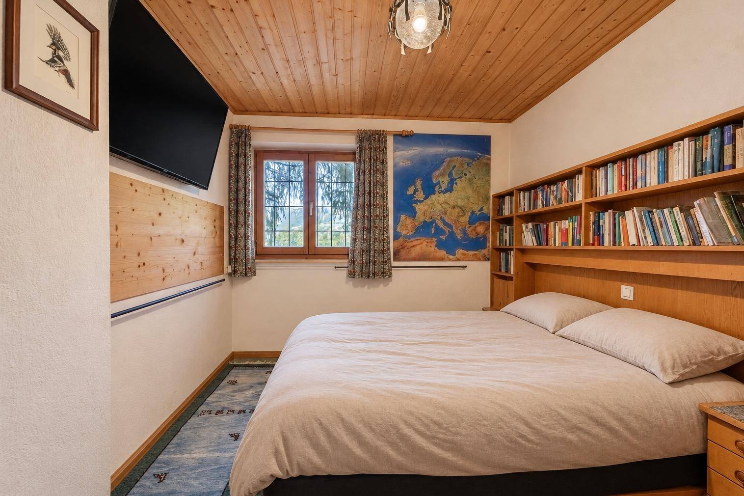 Helles Schlafzimmer mit Holzwänden, Bücherregal und Blick ins Grüne.